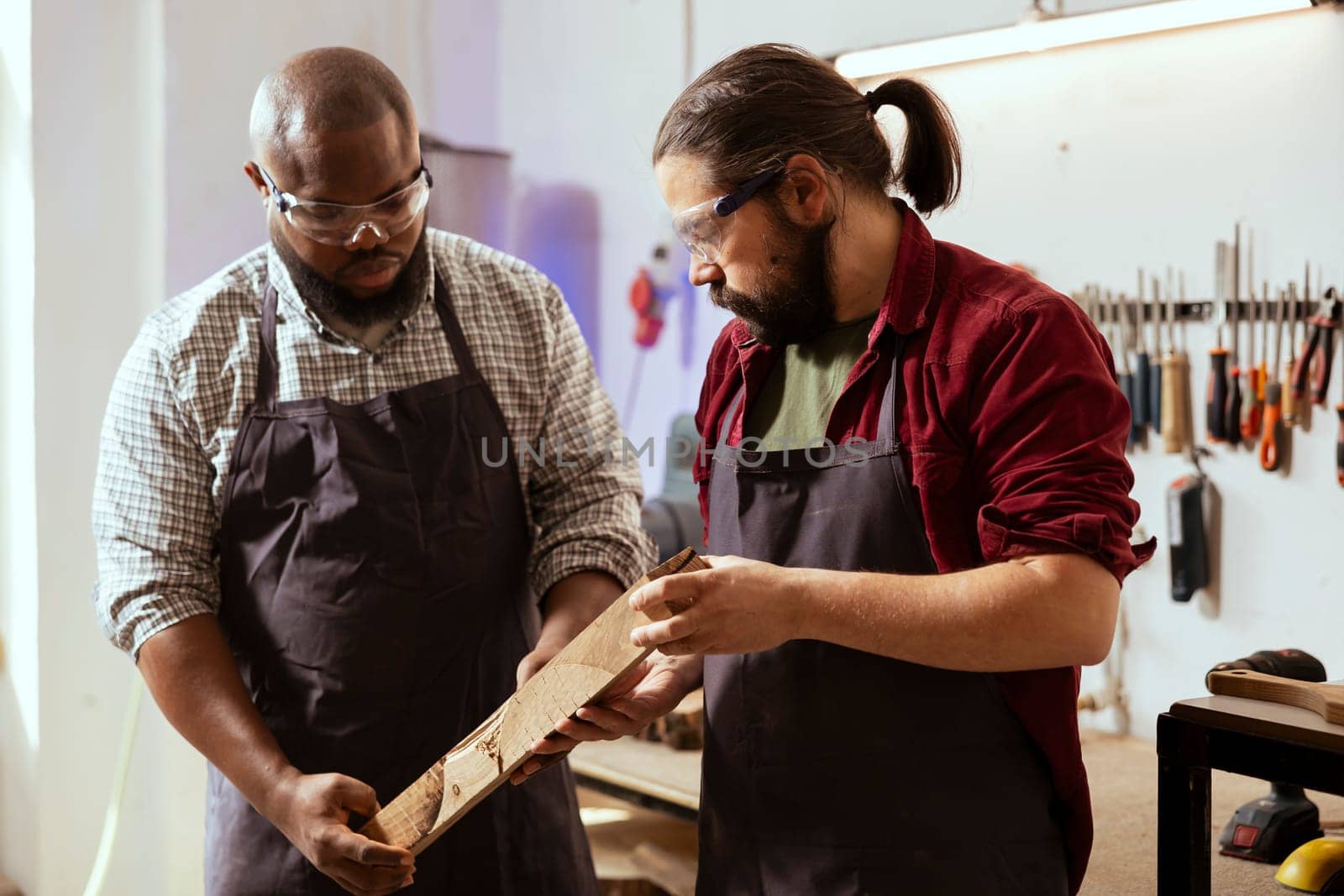 Woodworker holding timber block, brainstorming with colleague next steps in wood processing. Manufacturer and BIPOC apprentice analyzing piece of wood together, sizing it up