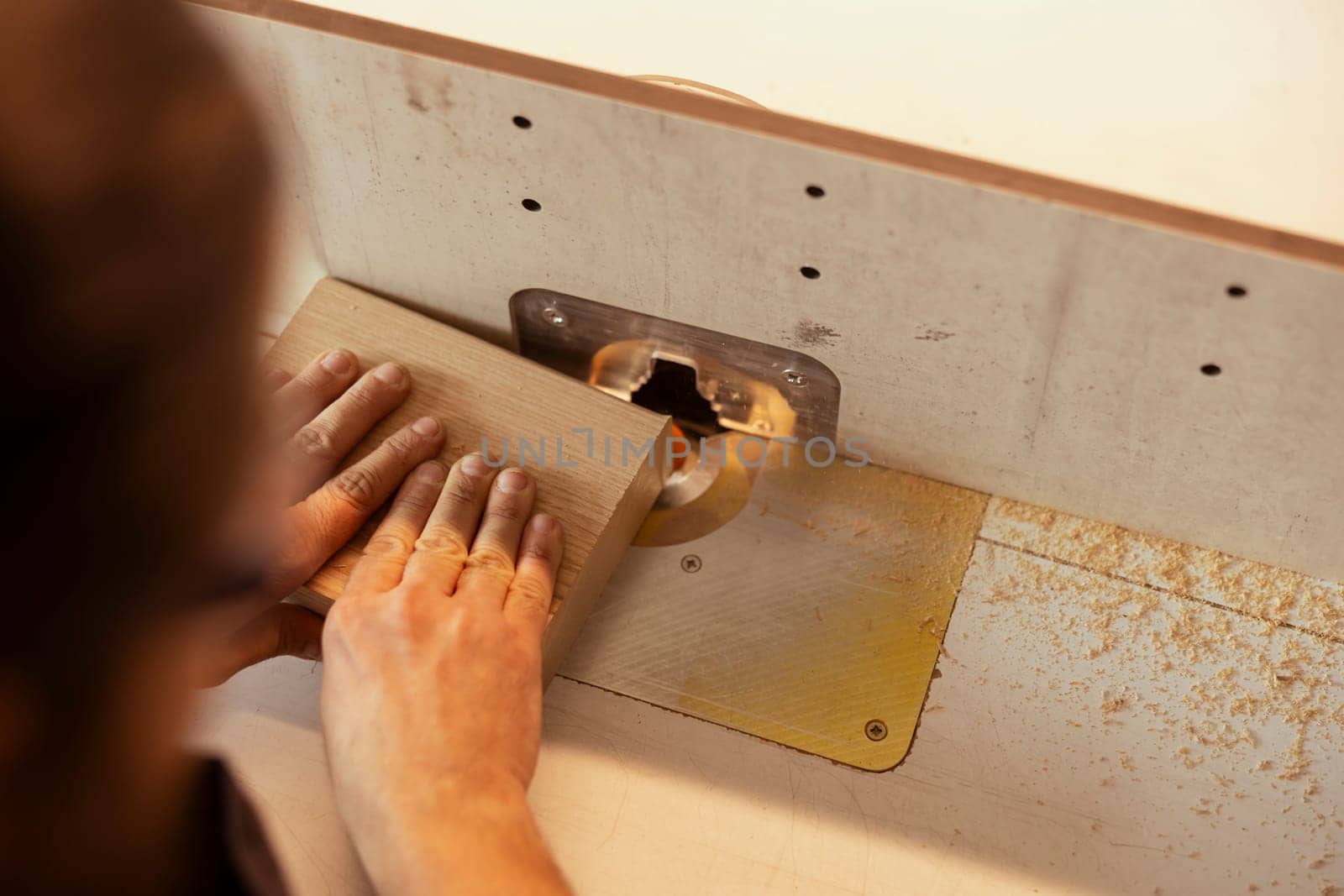 Carpenter in studio puts wood block through spindle moulder, close up by DCStudio