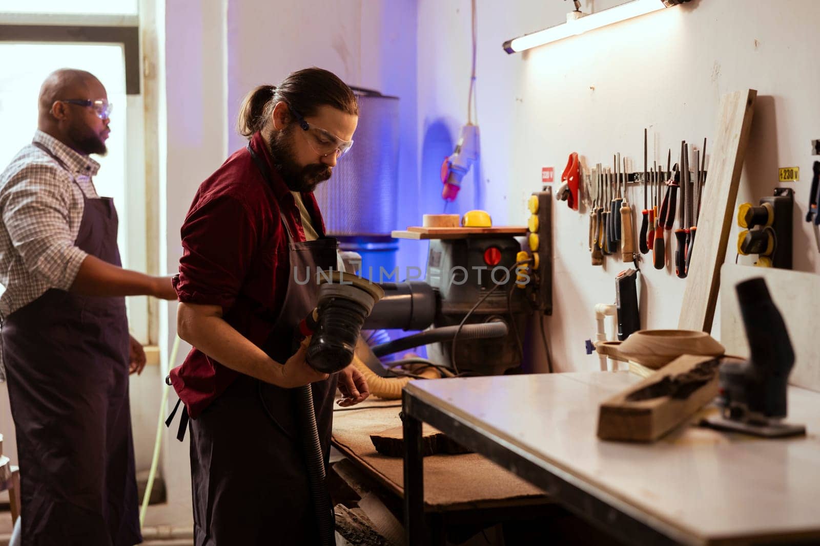 Woodworking expert in carpentry shop inspecting damaged angle grinder by DCStudio