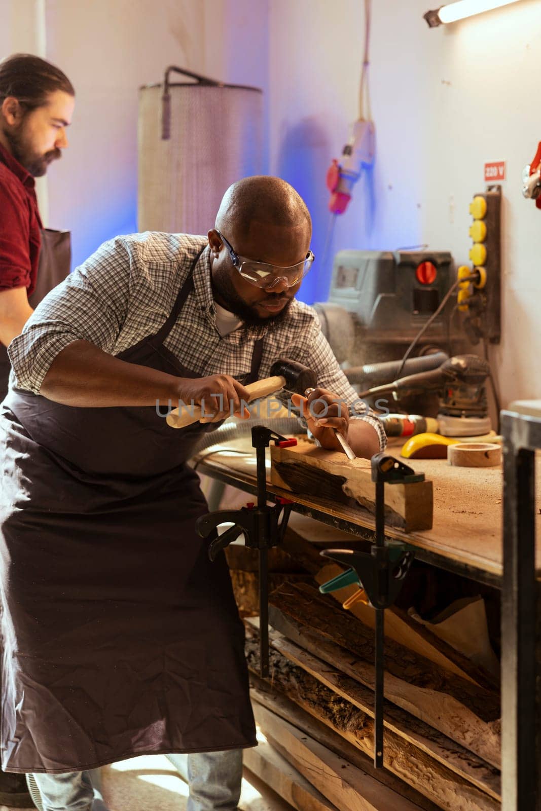 African american manufacturer carving intricate designs into wood using chisel and hammer in carpentry shop. BIPOC artisan in woodworking workshop shaping wooden pieces with tools, close up shot