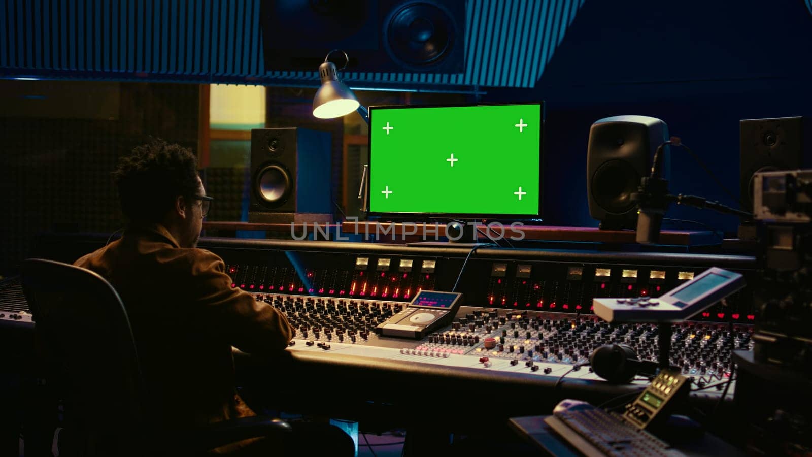 African american sound engineer working in control room with mixing console by DCStudio