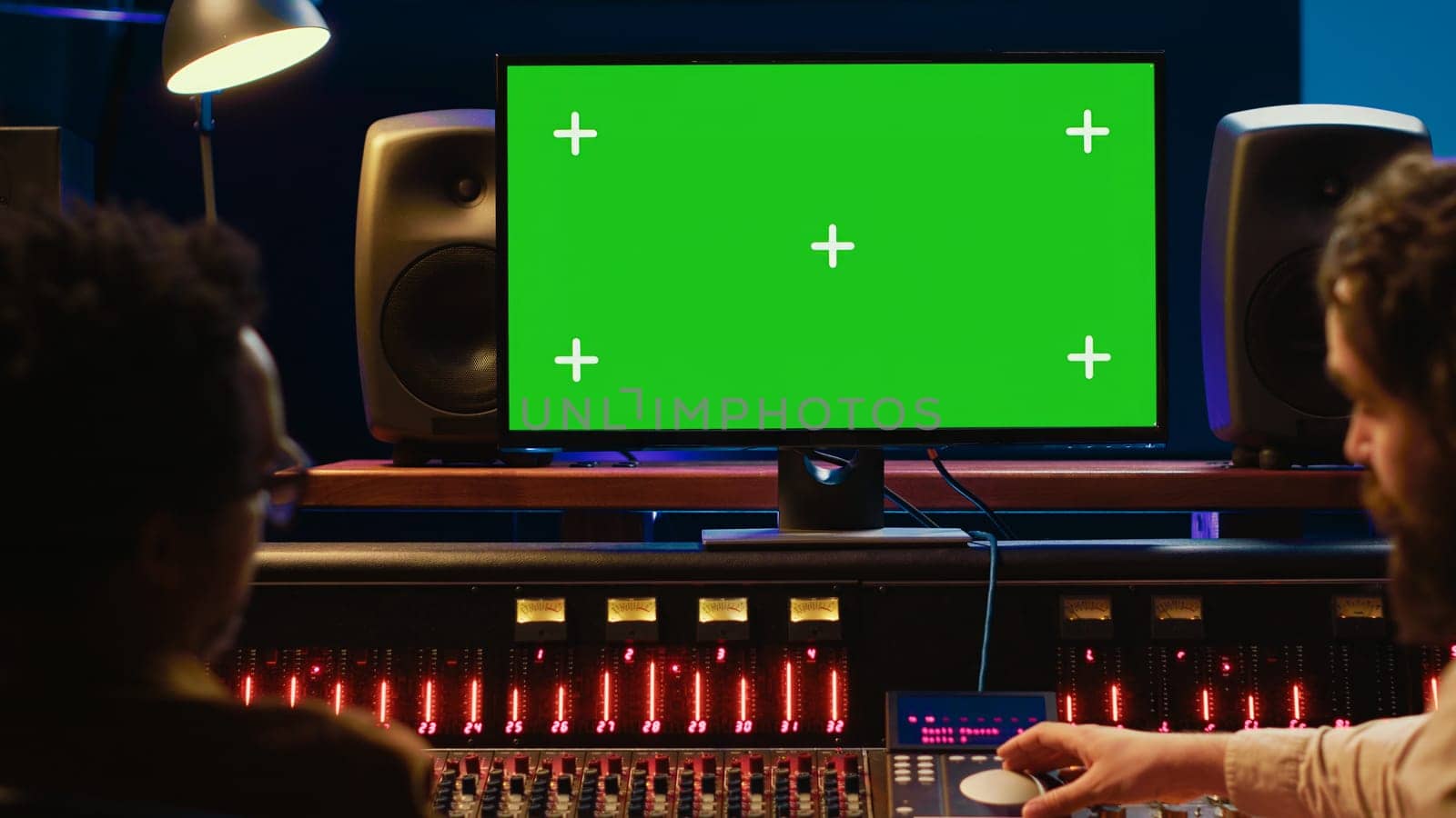 Diverse skilled artists working with isolated mockup display on pc, mixing and mastering tracks before creating a hit. People operating on control room console with knobs and sliders. Camera A.