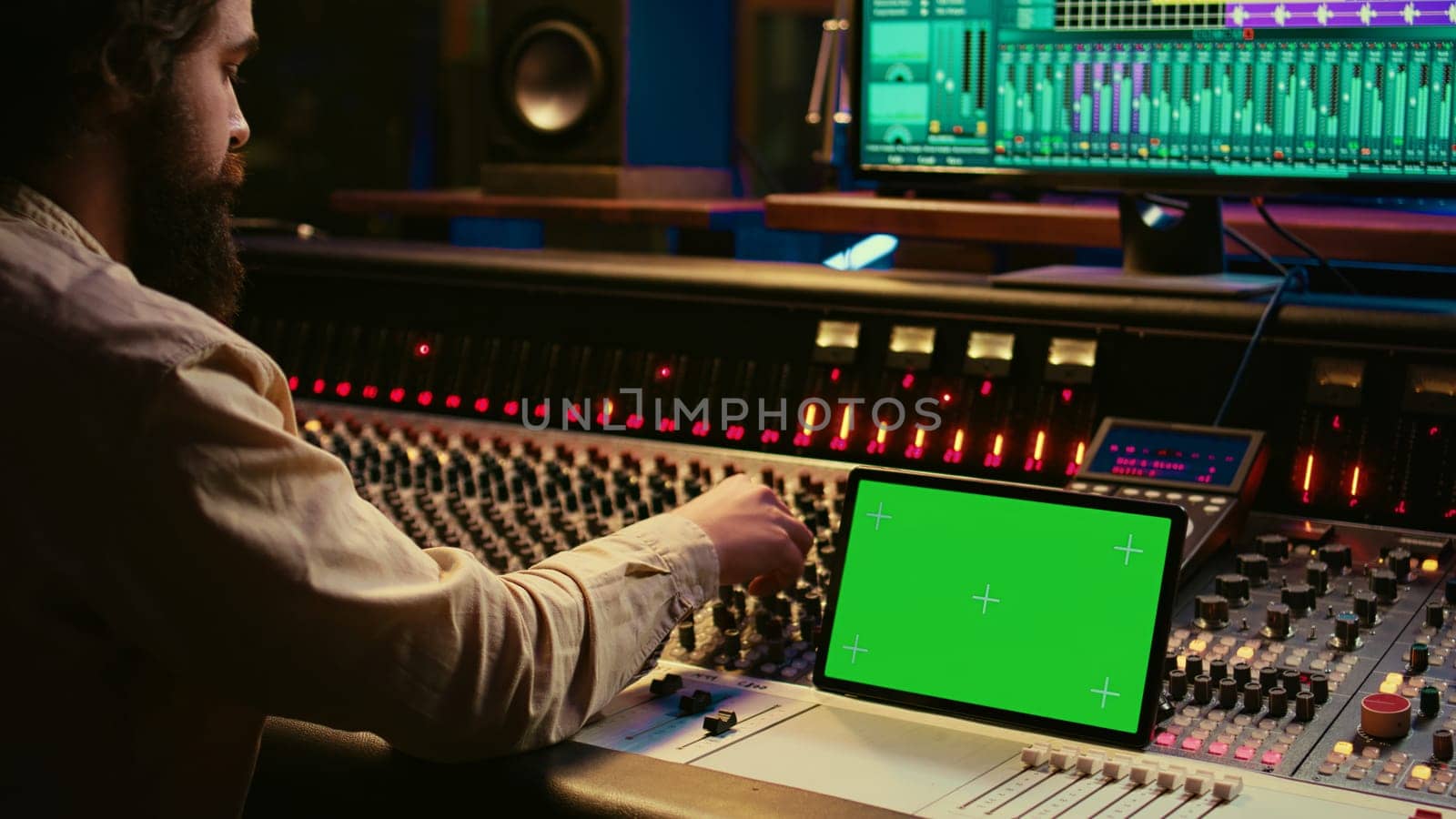 Audio expert mixing and mastering tunes on editing software next to greenscreen tablet, producing and recording tracks by pushing buttons and faders. Sound engineer in control room. Camera B.