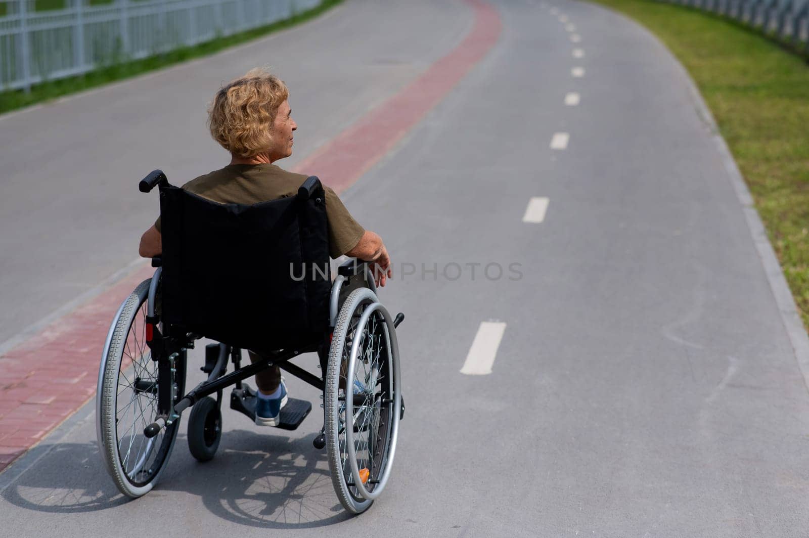 Rear view of an elderly woman in a wheelchair riding on a bike path