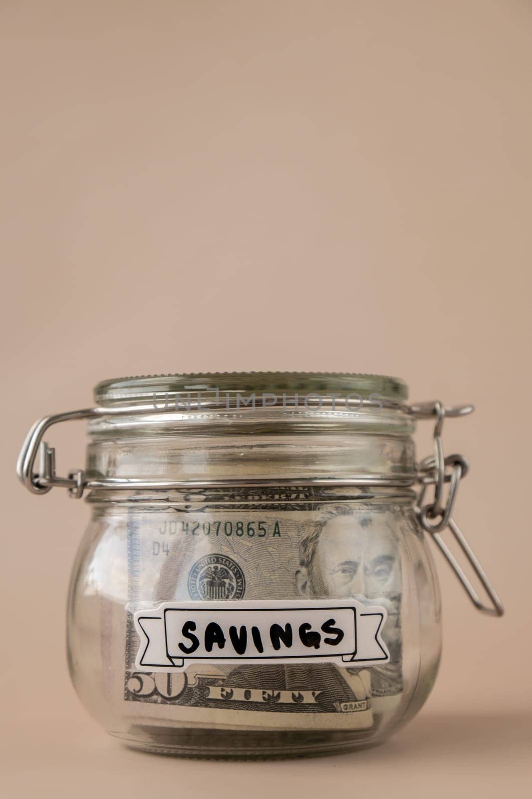 Saving Money In Glass Jar filled with Dollars banknotes. SAVINGS transcription in front of jar. Managing personal finances extra income for future insecurity. Beige background