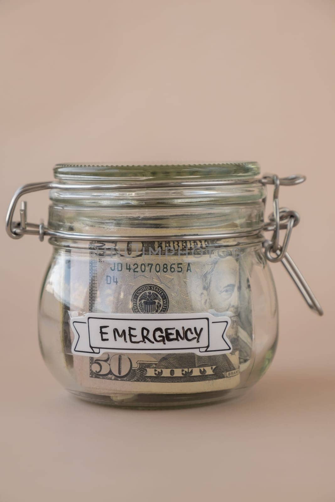 Saving Money In Glass Jar filled with Dollars banknotes. EMERGENCY transcription in front of jar. Managing personal finances extra income for future insecurity by anna_stasiia