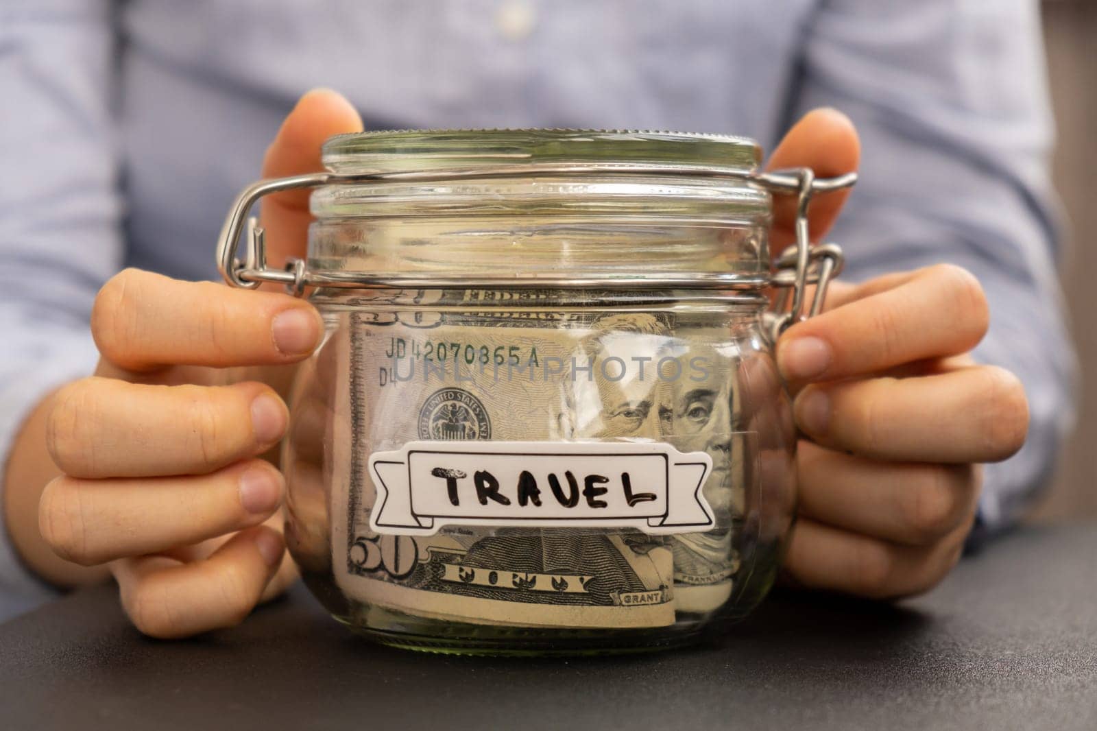 Unrecognizable woman holding Saving Money In Glass Jar filled with Dollars banknotes. TRAVEL transcription in front of jar. Managing personal finances extra income for future insecurity by anna_stasiia