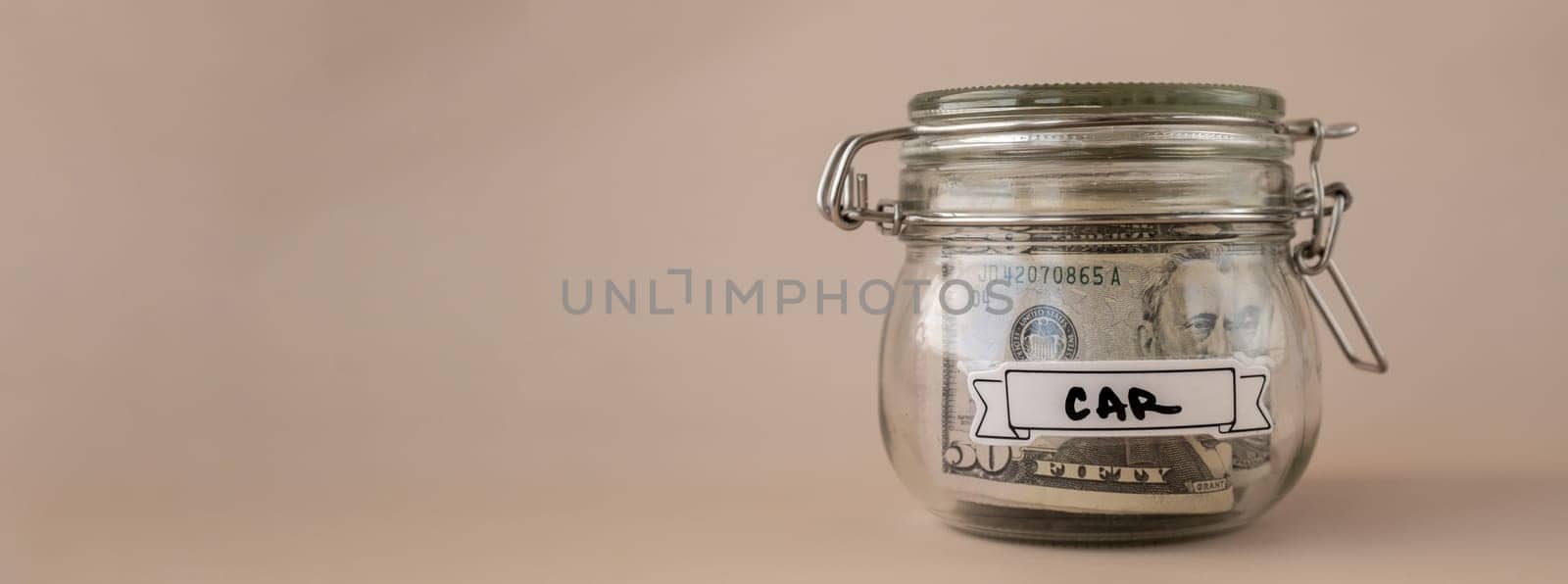 Saving Money In Glass Jar filled with Dollars banknotes. CAR transcription in front of jar. Managing personal finances extra income for future insecurity by anna_stasiia