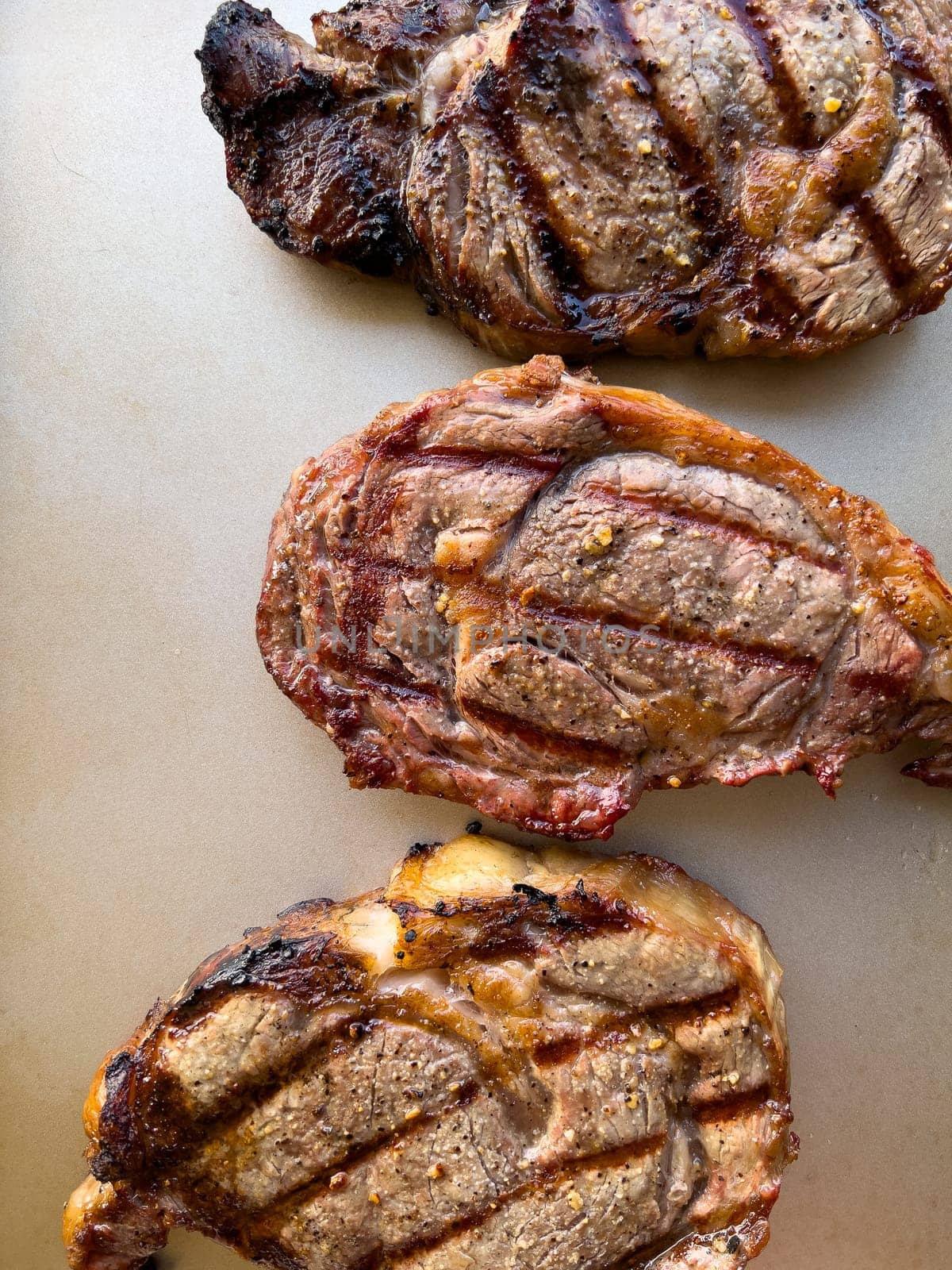 succulent texture of three ribeye steaks grilled to perfection, featuring charred edges and distinct grill marks, showcased on a neutral background.