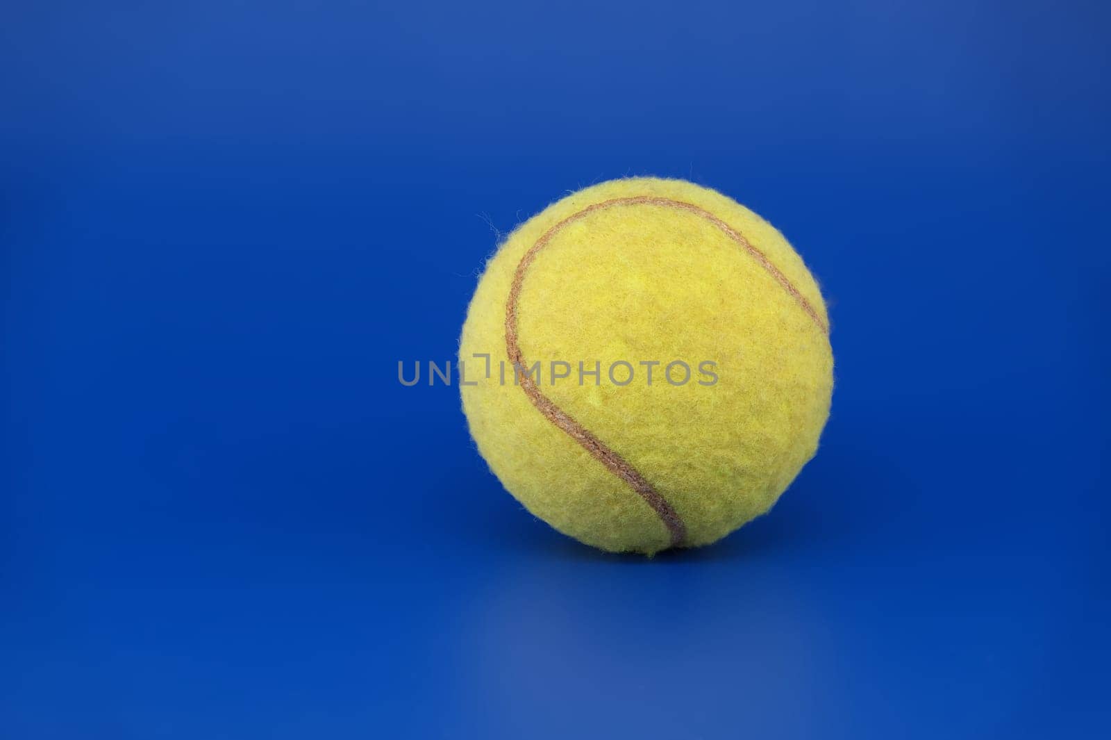 Yellow tennis ball on a bright blue background with free copy space in close up view