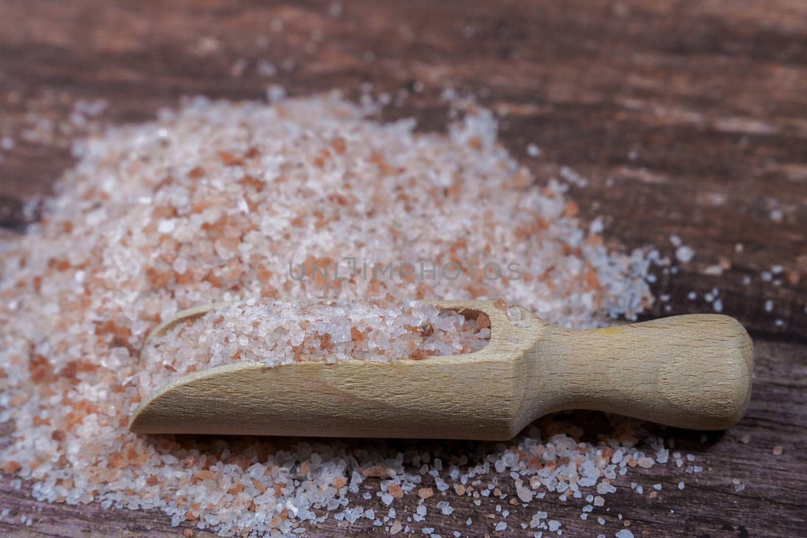 close-up of a pile of pink himalayan salt in a wooden spoon on a wooden table with copy space