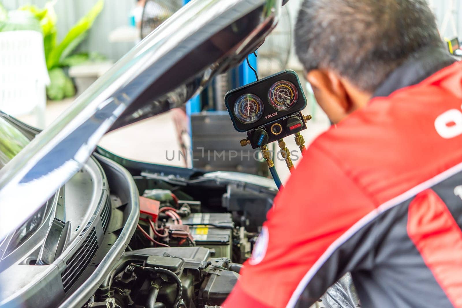 Bangkok, Thailand - May 4, 2023 : Unidentified car mechanic or serviceman refilling air condition and checking a air compressor for fix and repair problem at car garage or repair shop