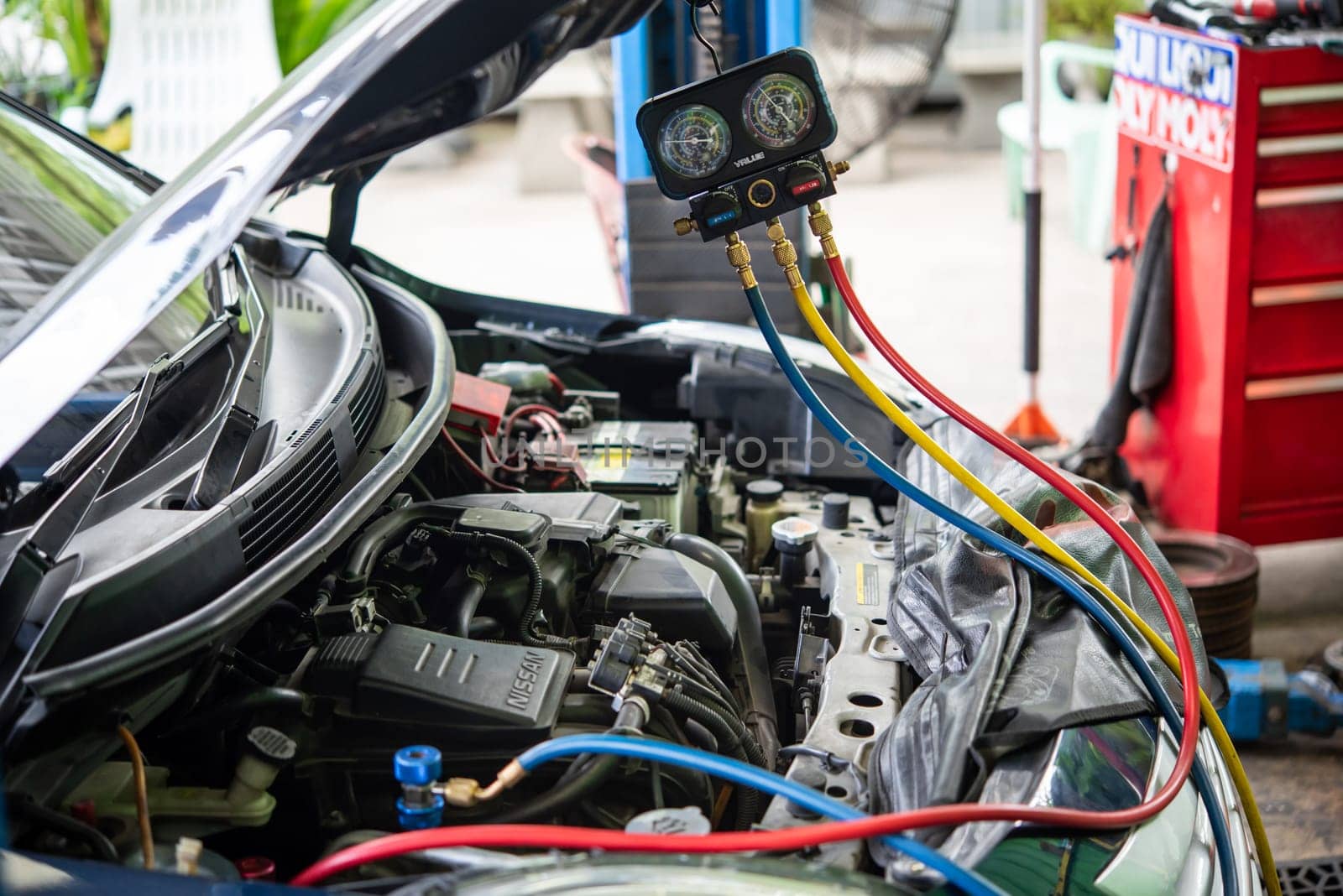 Bangkok, Thailand - May 4, 2023 : Unidentified car mechanic or serviceman refilling air condition and checking a air compressor for fix and repair problem at car garage or repair shop