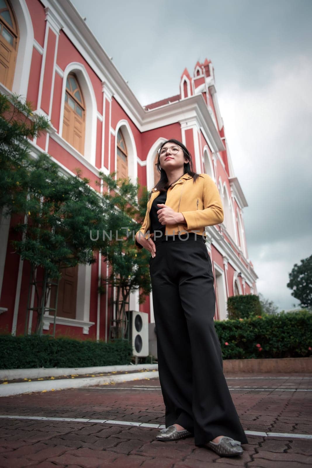 Beautiful asian woman (LGBTQ) natural makeup wear fashion yellow leather clothes with glasses posing at old town and vintage building outdoor fashion style