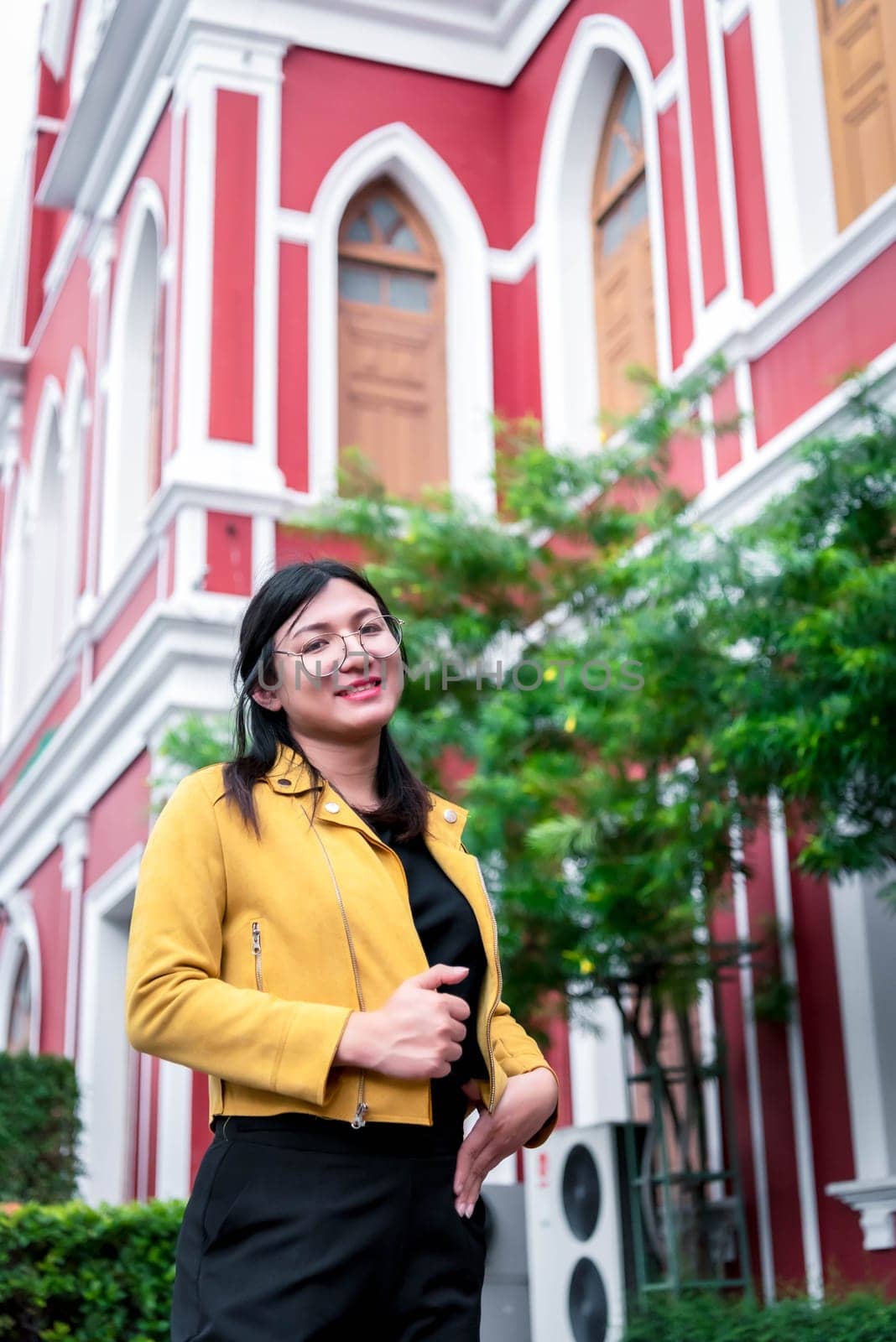 Beautiful asian woman (LGBTQ) natural makeup wear fashion yellow leather clothes with glasses posing at old town and vintage building outdoor fashion style