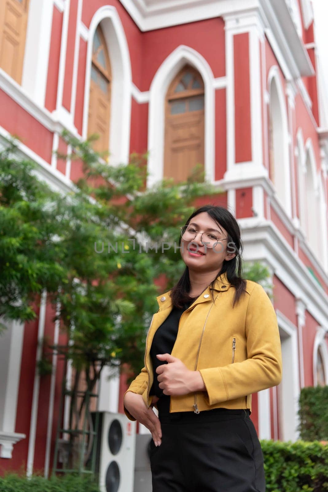 Beautiful asian woman (LGBTQ) natural makeup wear fashion yellow leather clothes with glasses posing at old town and vintage building outdoor fashion style