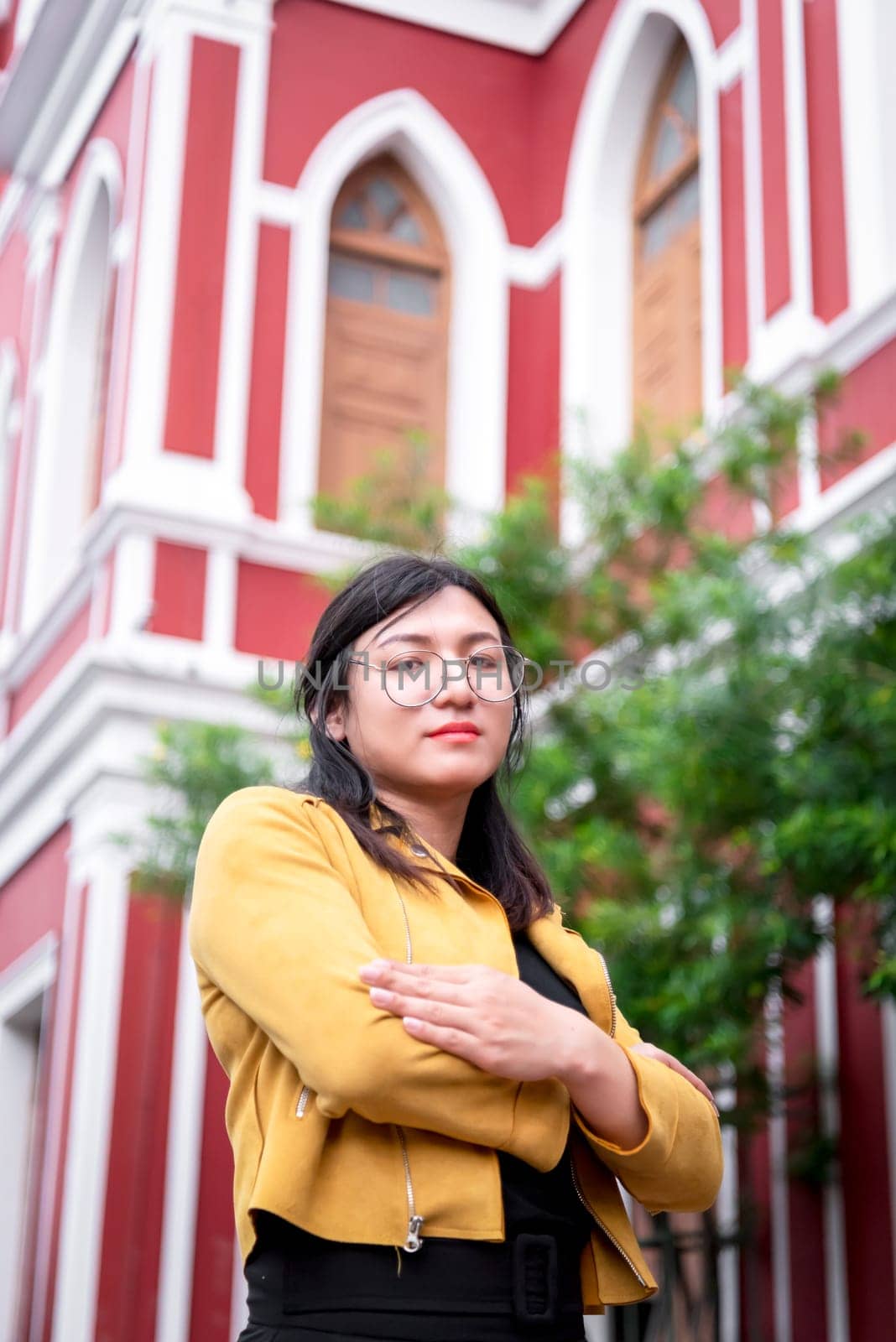 Beautiful asian woman (LGBTQ) natural makeup wear fashion yellow leather clothes with glasses posing at old town and vintage building outdoor fashion style