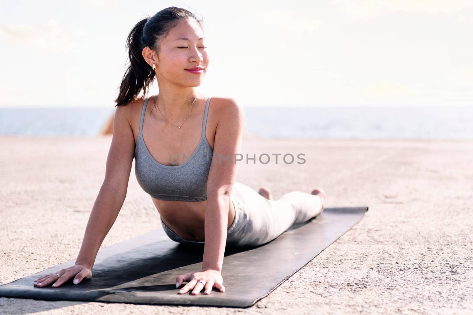 young asian woman in sportswear doing yoga by the sea, concept of mental relaxation and healthy lifestyle, copy space for text