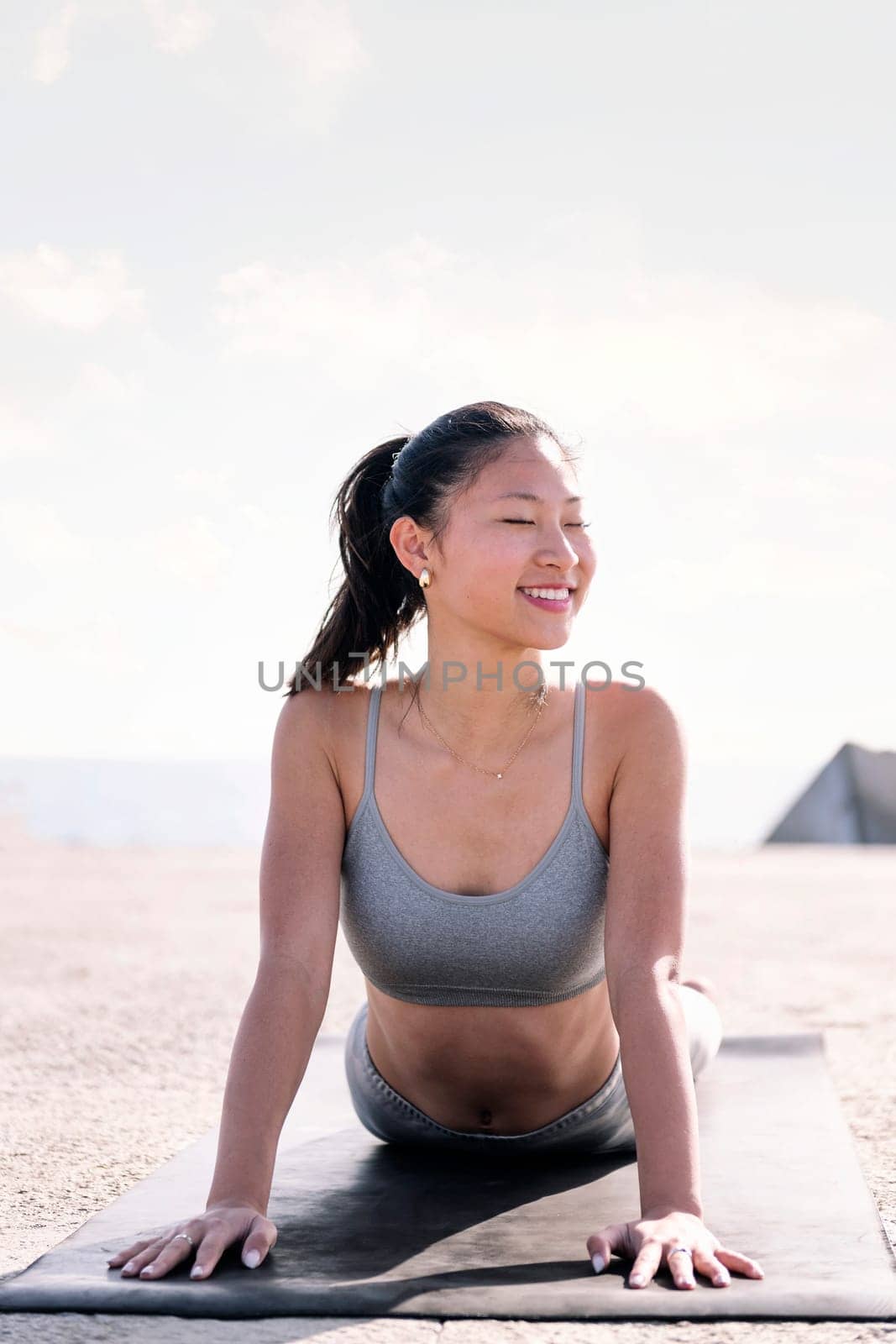 young asian woman in sportswear doing yoga by the sea, concept of mental relaxation and healthy lifestyle, copy space for text