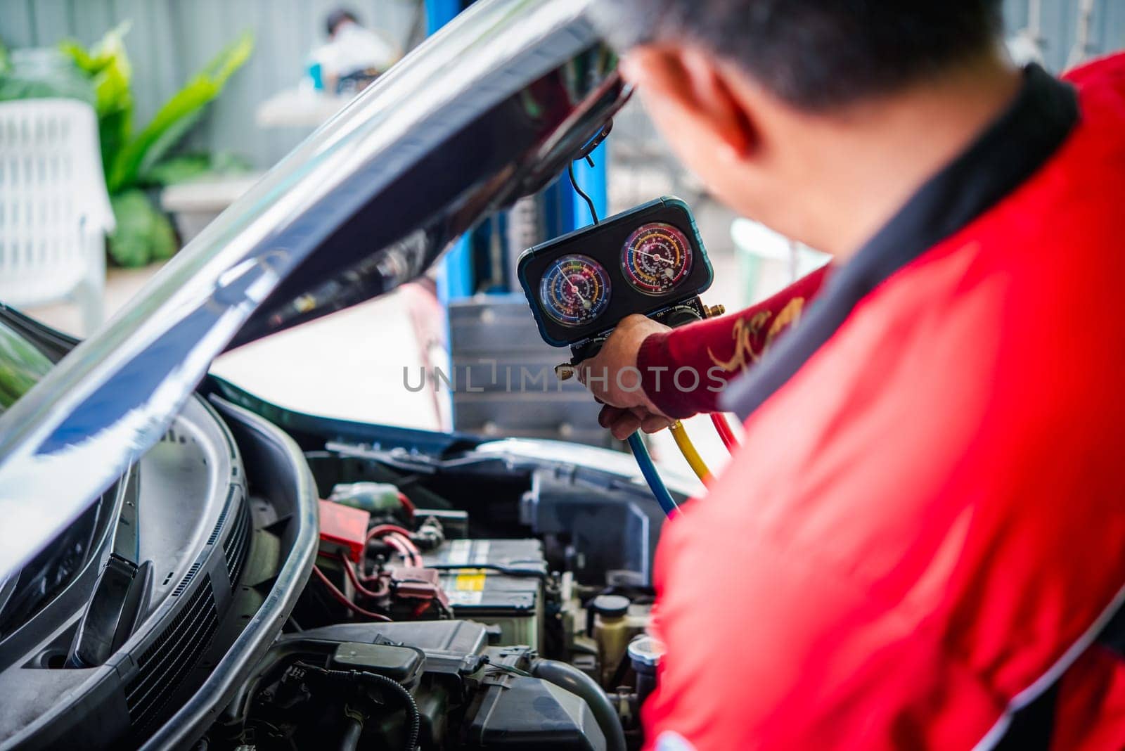 Car mechanic or serviceman refilling air condition and checking a air compressor for fix and repair problem at car garage or repair shop