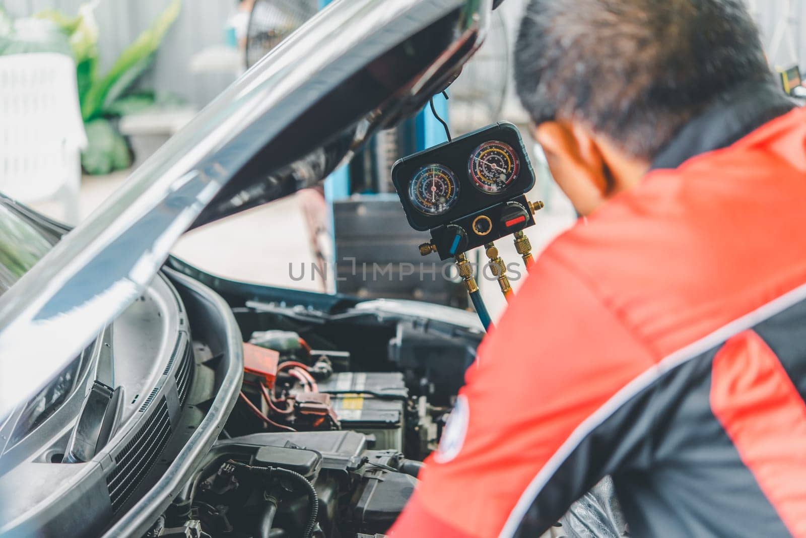 Car mechanic or serviceman refilling air condition and checking a air compressor for fix and repair problem at car garage or repair shop