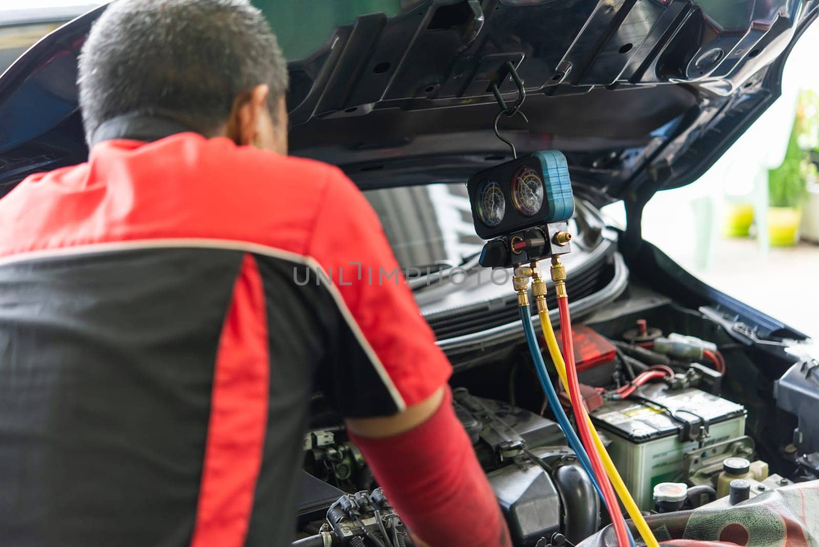 Car mechanic or serviceman refilling air condition and checking a air compressor for fix and repair problem at car garage or repair shop