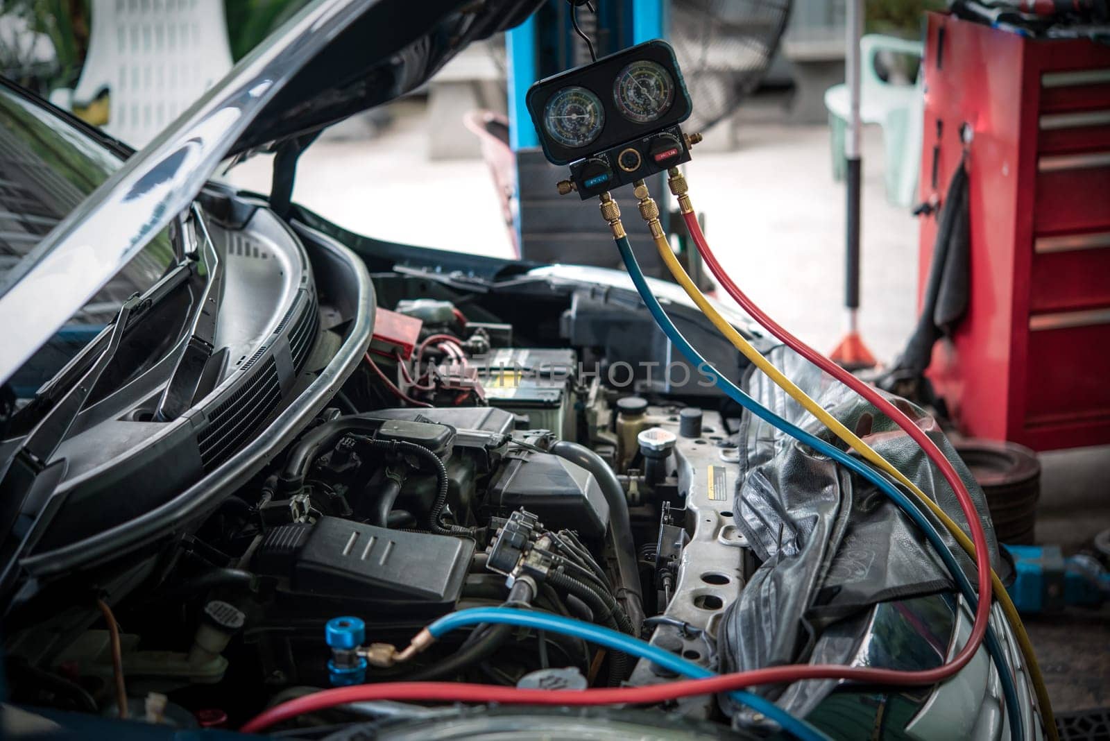 Car mechanic or serviceman refilling air condition and checking a air compressor for fix and repair problem at car garage or repair shop