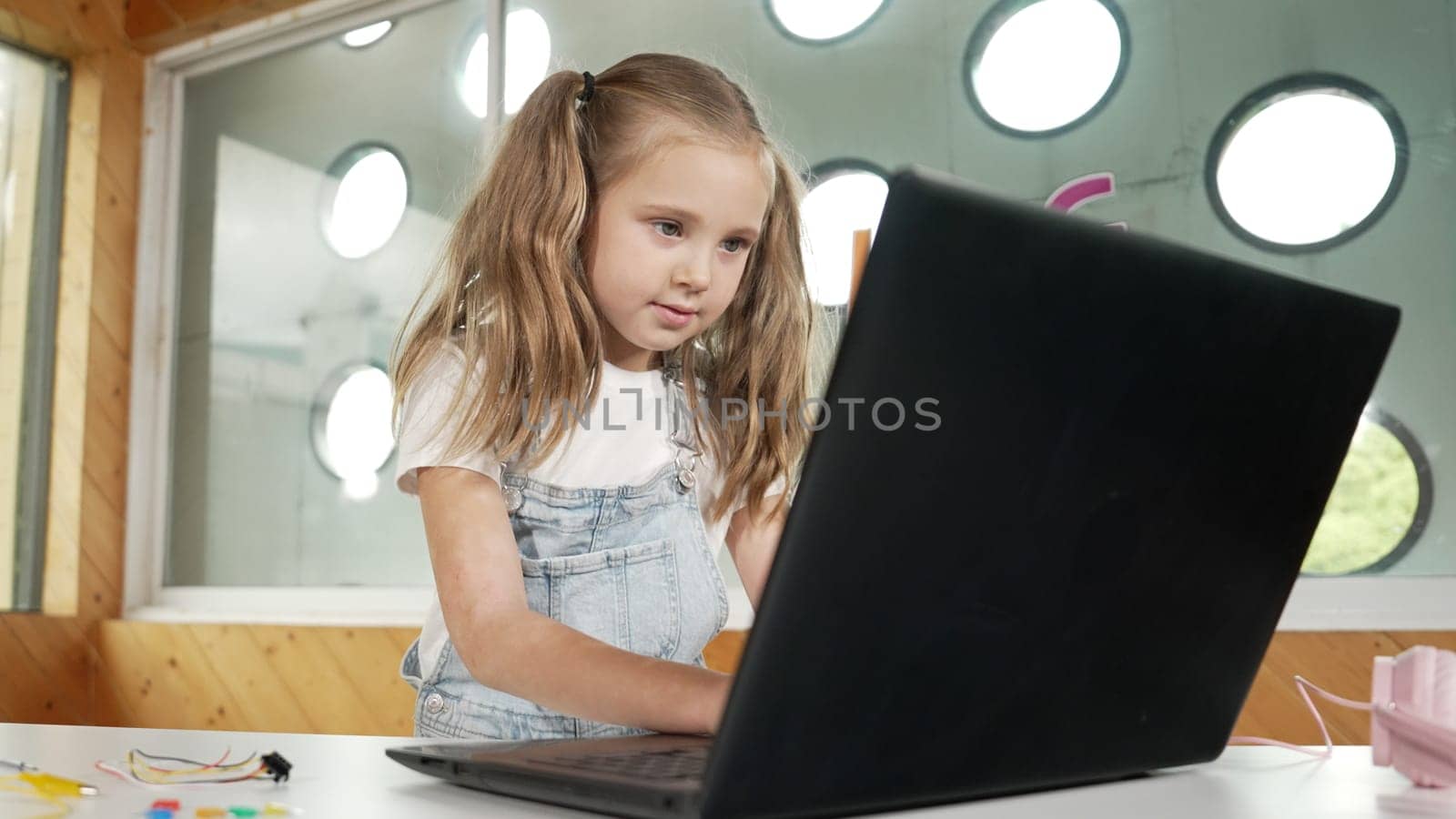 Young student working on laptop or studying in online classroom. Caucasian girl typing on laptop while doing homework or listening music.Little kid wearing headphone. Creative learning. Erudition.