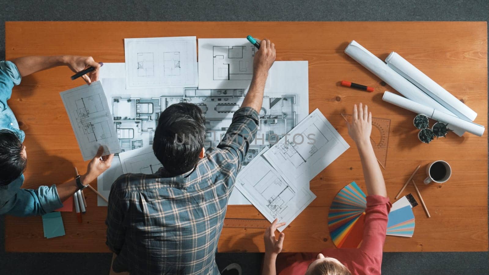 Group of people looking at blueprint while brainstorming idea. Top view of engineer team looking and planning house construction by using blueprint. Engineer hold paper while point at plan. Symposium.