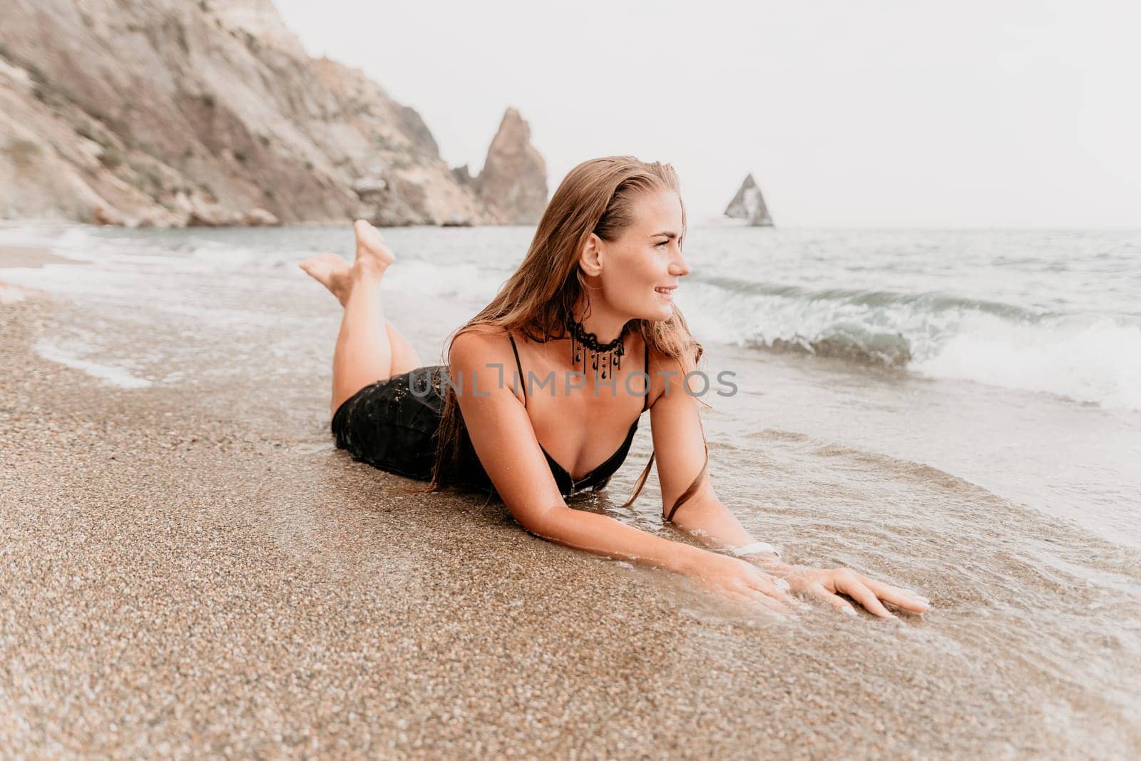 Woman travel sea. Young Happy woman in a long red dress posing on a beach near the sea on background of volcanic rocks, like in Iceland, sharing travel adventure journey