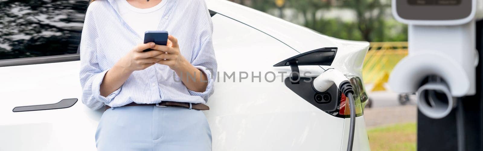 Young woman using smartphone to pay for electric car charging. Exalt by biancoblue