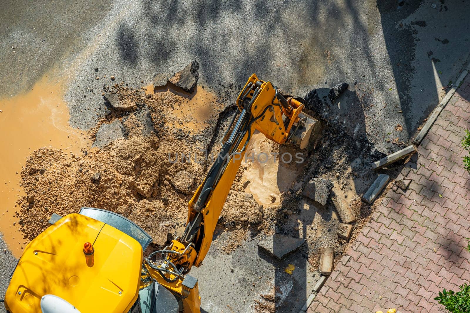 Digger digging asphalt to repair a water fault in a street by Sonat