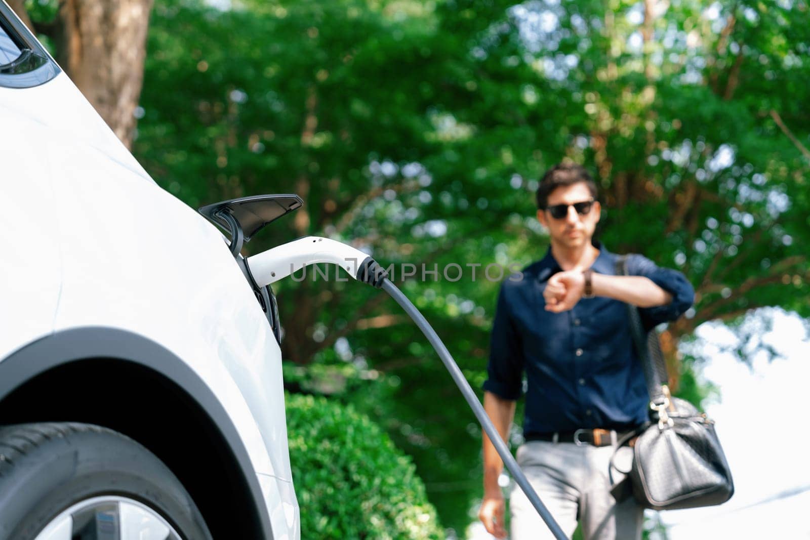 Young man recharge electric car's battery from charging station. Expedient by biancoblue