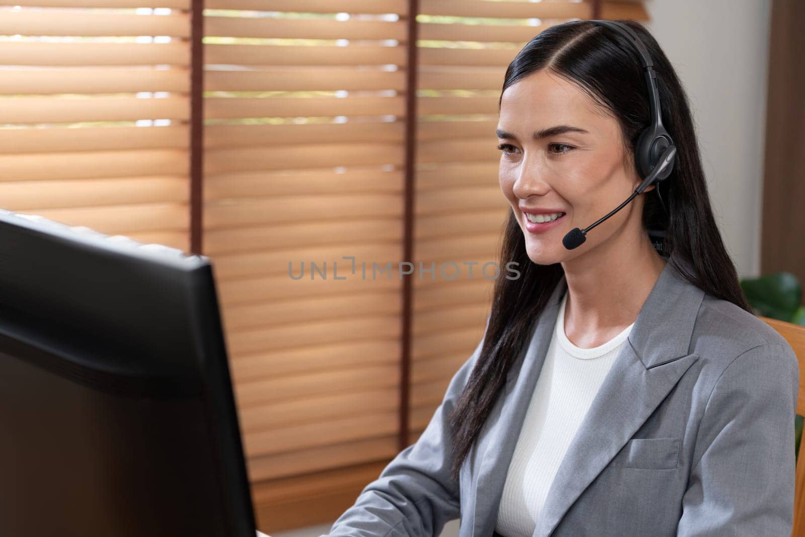 Female call center operator or customer service helpdesk staff working on workspace while talking on the headset to provide assistance for customer. Professional modern business service. Blithe