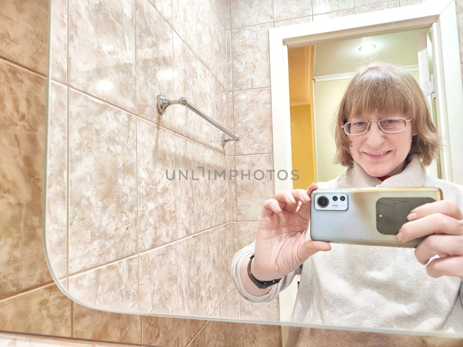 Mature woman captures her reflection while taking selfie. The reflection of middle aged girl with a phone in the mirror. Partial focus