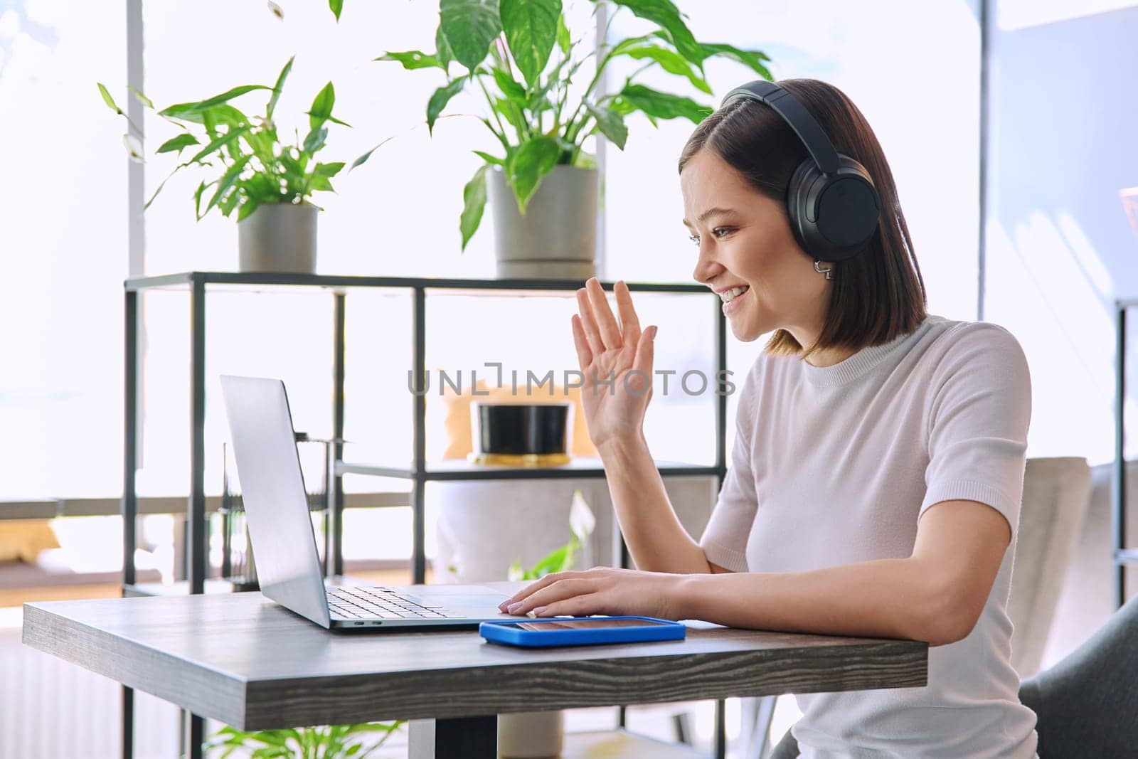 Young woman in headphones having work video chat conference call, using laptop in cafe by VH-studio