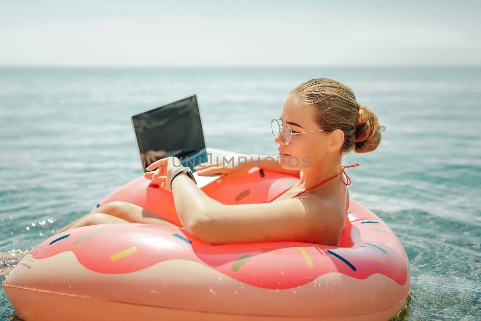 Woman laptop sea. Freelancer woman in sunglases floating on an inflatable big pink donut with a laptop in the sea. People summer vacation rest lifestyle concept by Matiunina