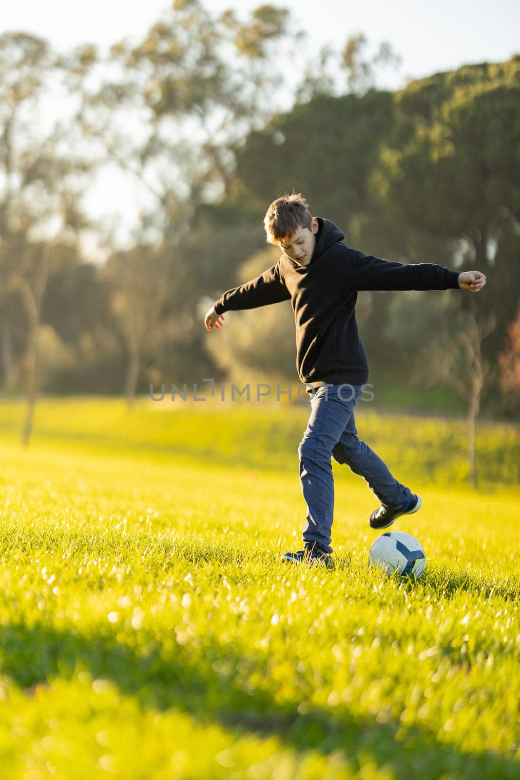 A boy is playing soccer in a field. He is wearing a black hoodie and gray pants