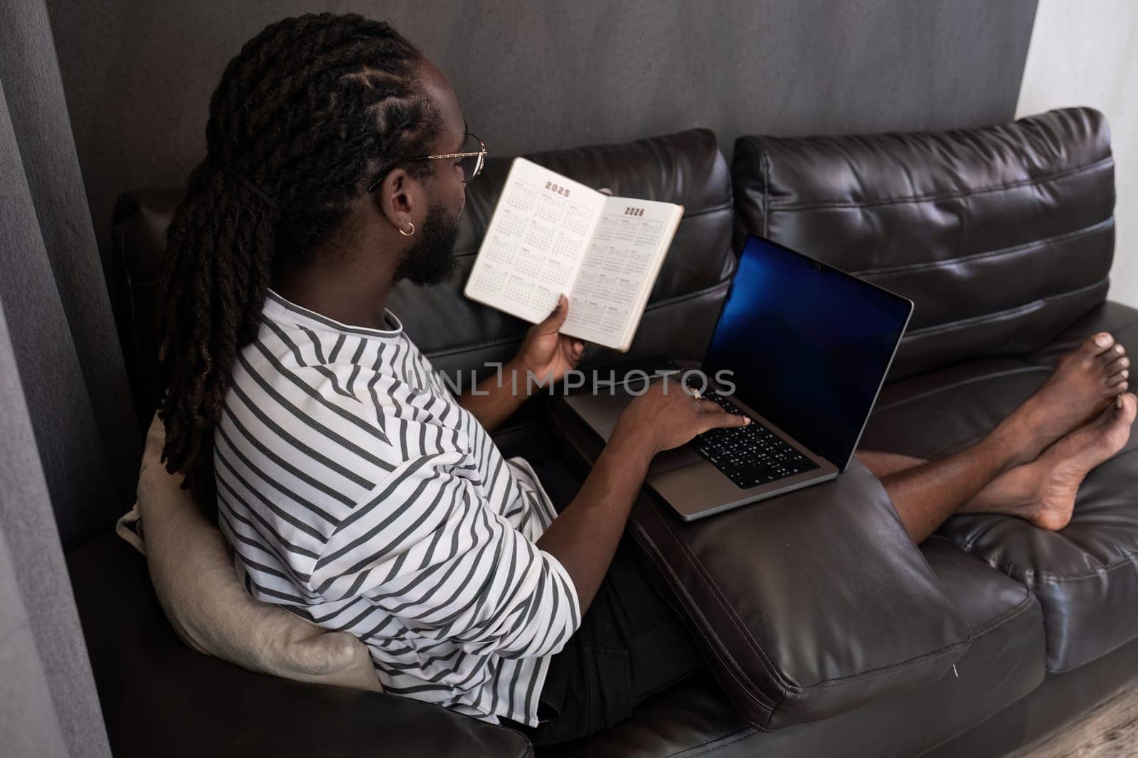 Young African American businessman spends his weekend working from home using his laptop in the living room. by wichayada