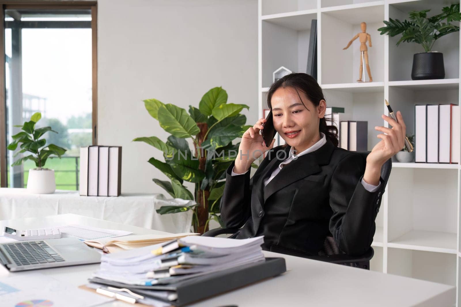 Asian female accountant Discussing business over the phone in an office with work plan documents on the table by wichayada