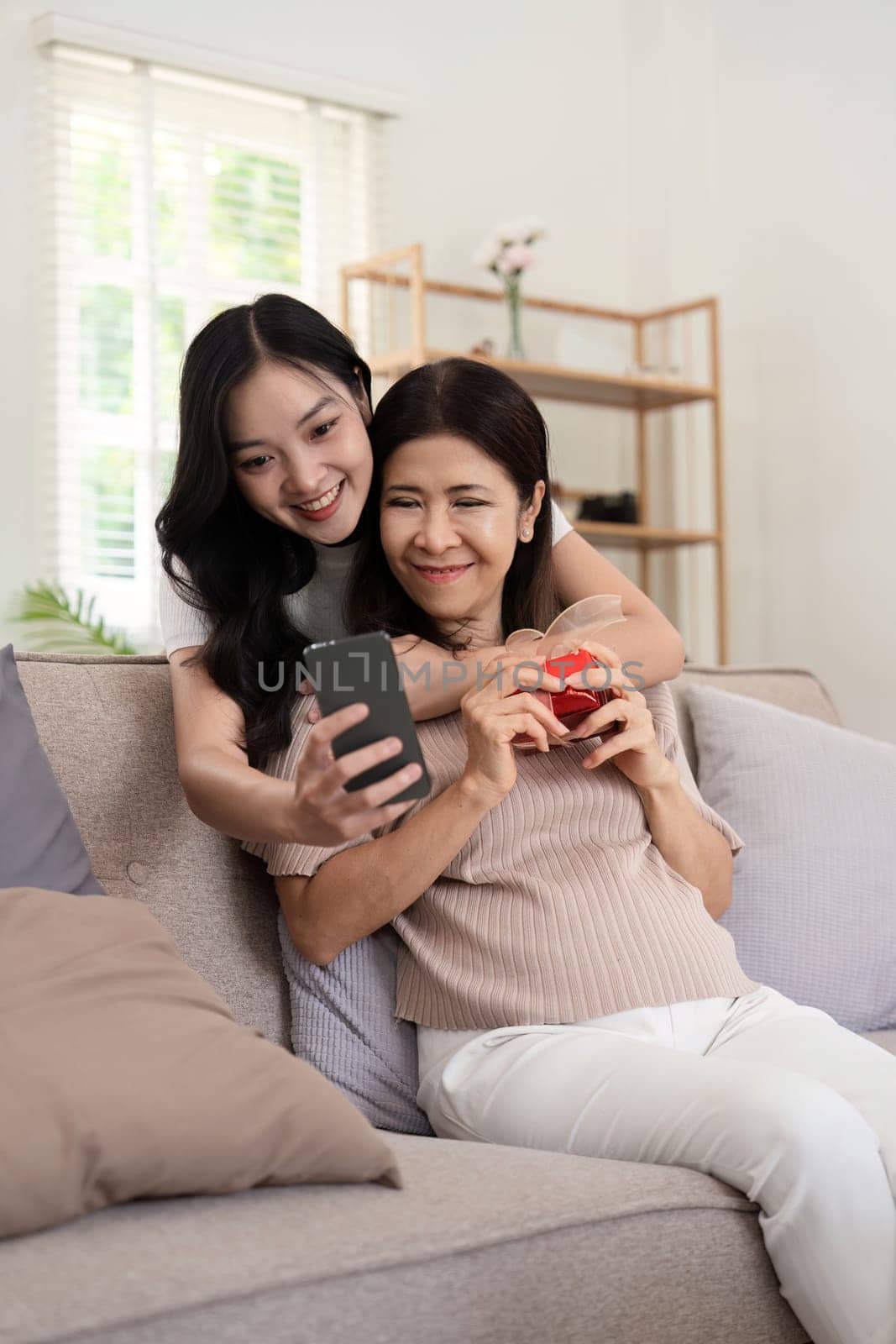 Daughter adult taking selfie using mobile phone with senior mother at home by nateemee
