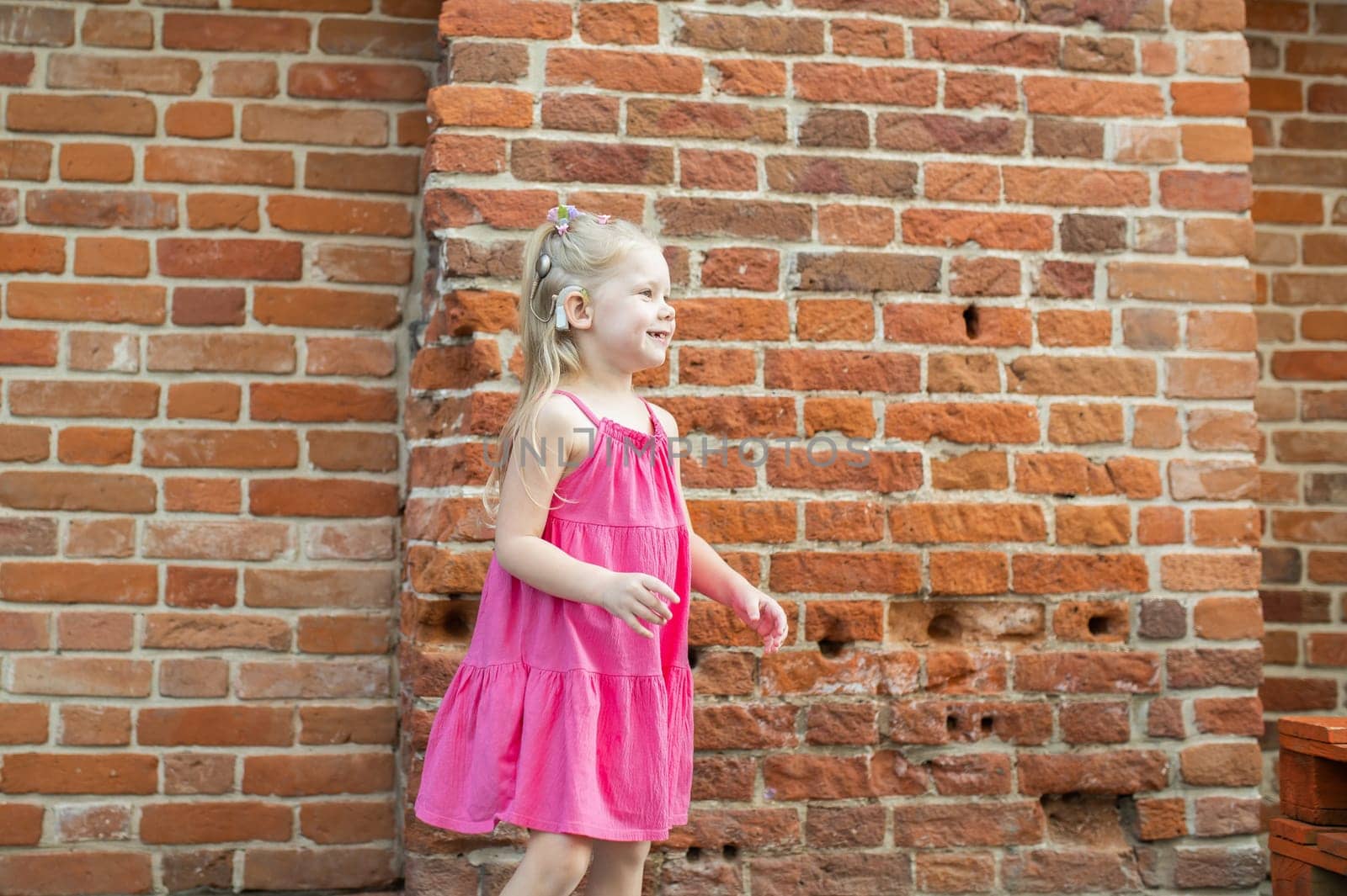 Child girl walks and have fun outdoor with cochlear implant on the head. Hearing aid and treatment concept. Copy space vertical.