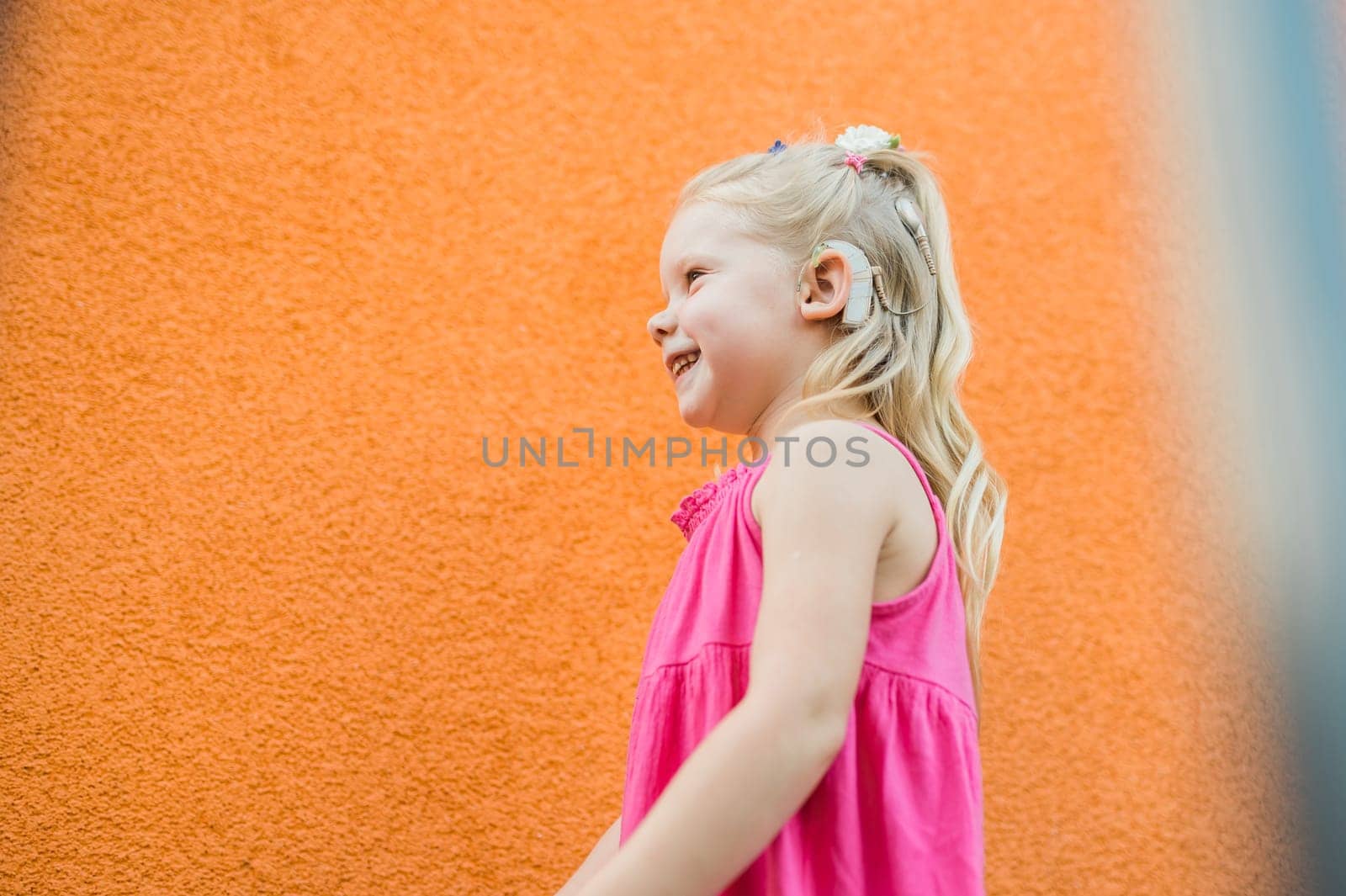 Child girl walks and have fun outdoor with cochlear implant on the head. Hearing aid and treatment concept. Copy space vertical. Inclusion by Satura86