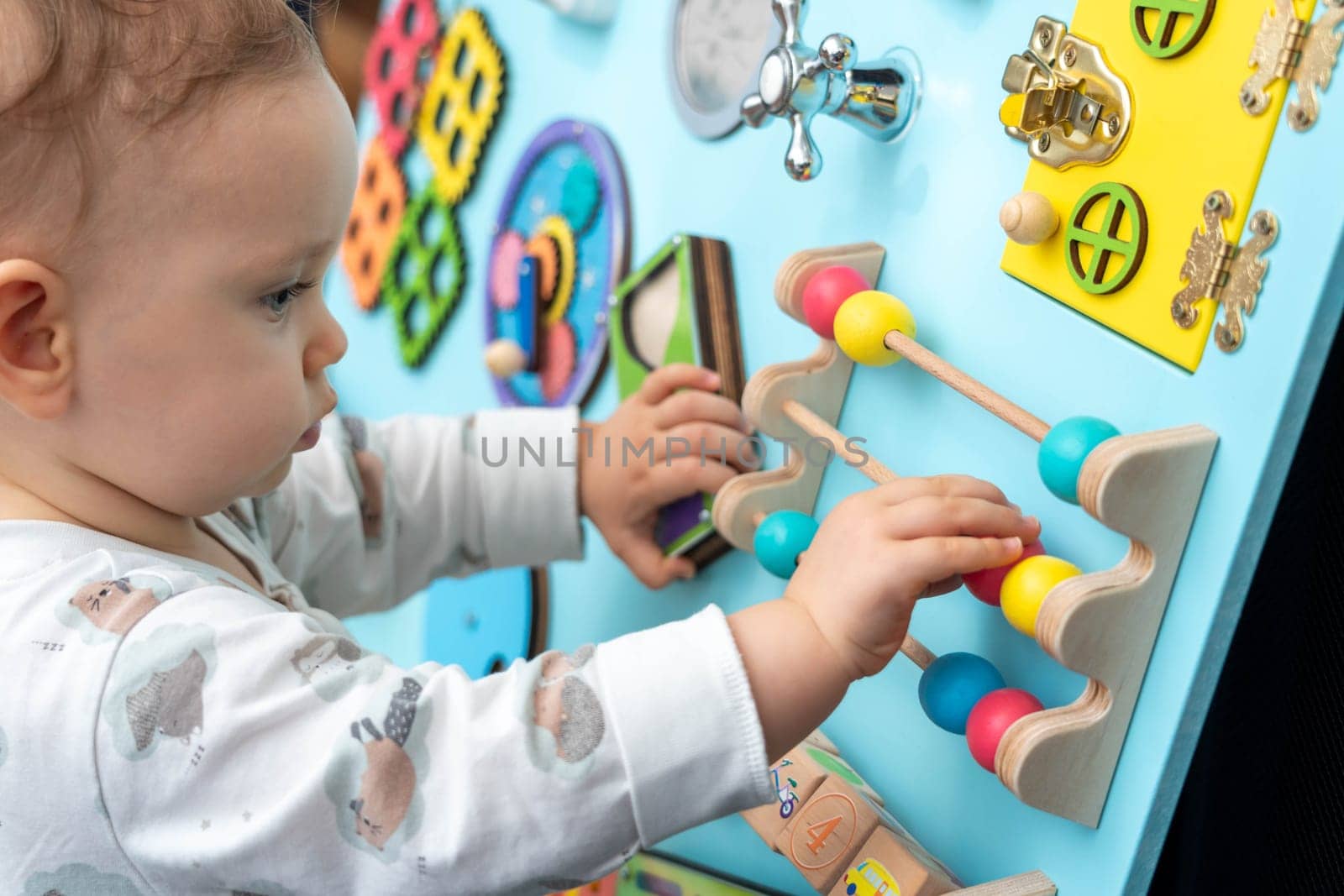 Cute little boy concentrates on moving round colored wooden elements on a busy board by sdf_qwe