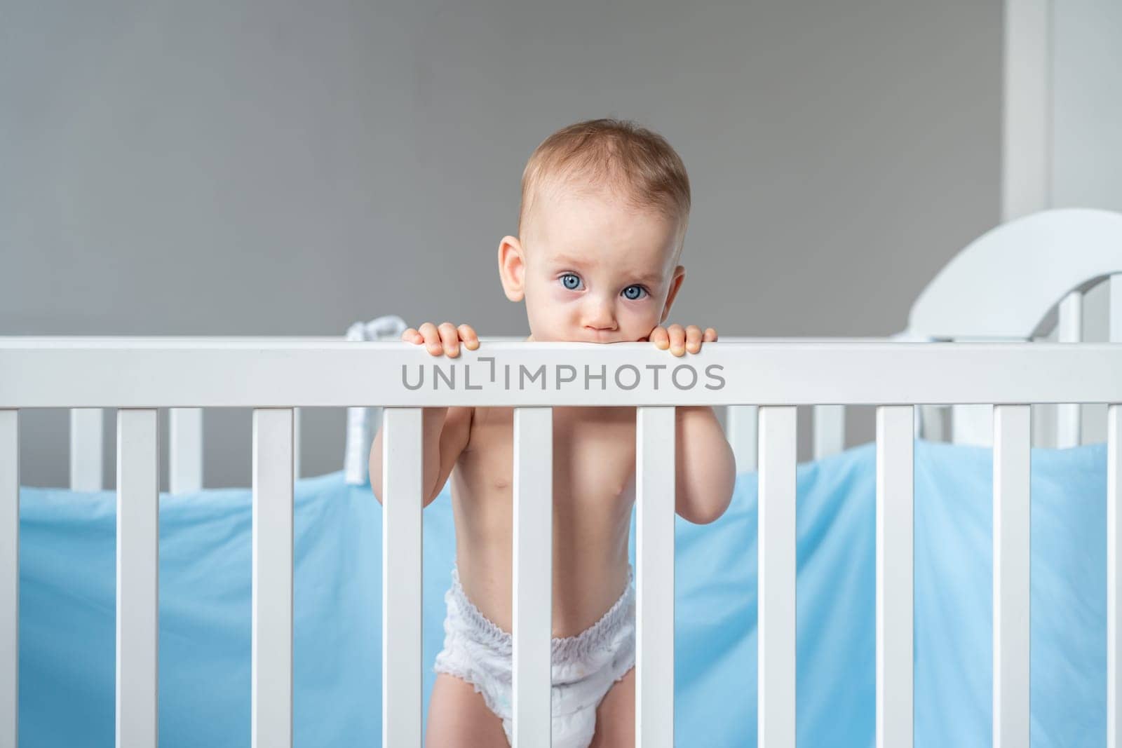 A baby in a diaper cutely bit the back of a wooden crib by sdf_qwe