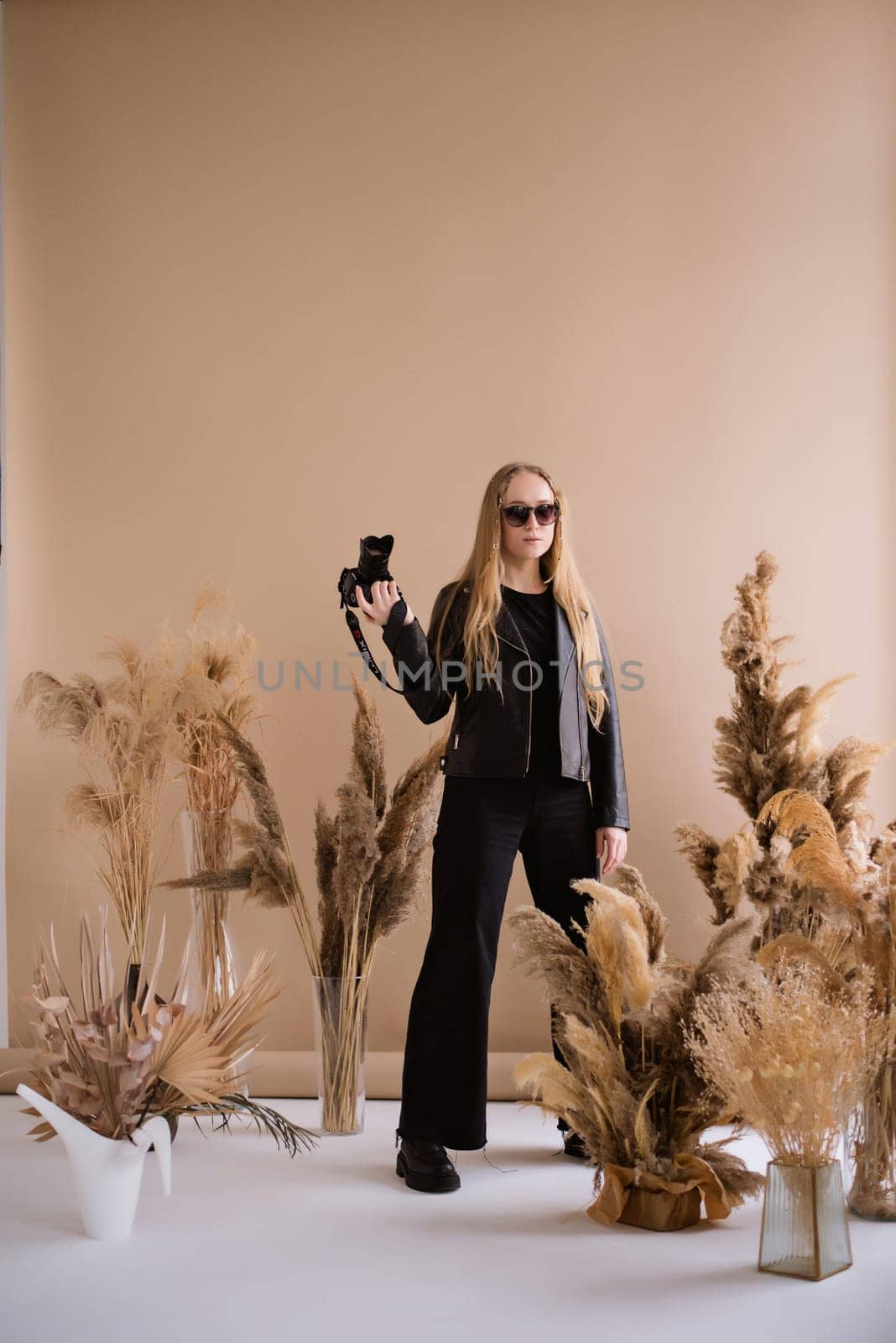 A crazy woman photographer, a blonde with a camera, happy and smiling in the production studio. Wearing a black clothes on a brown background