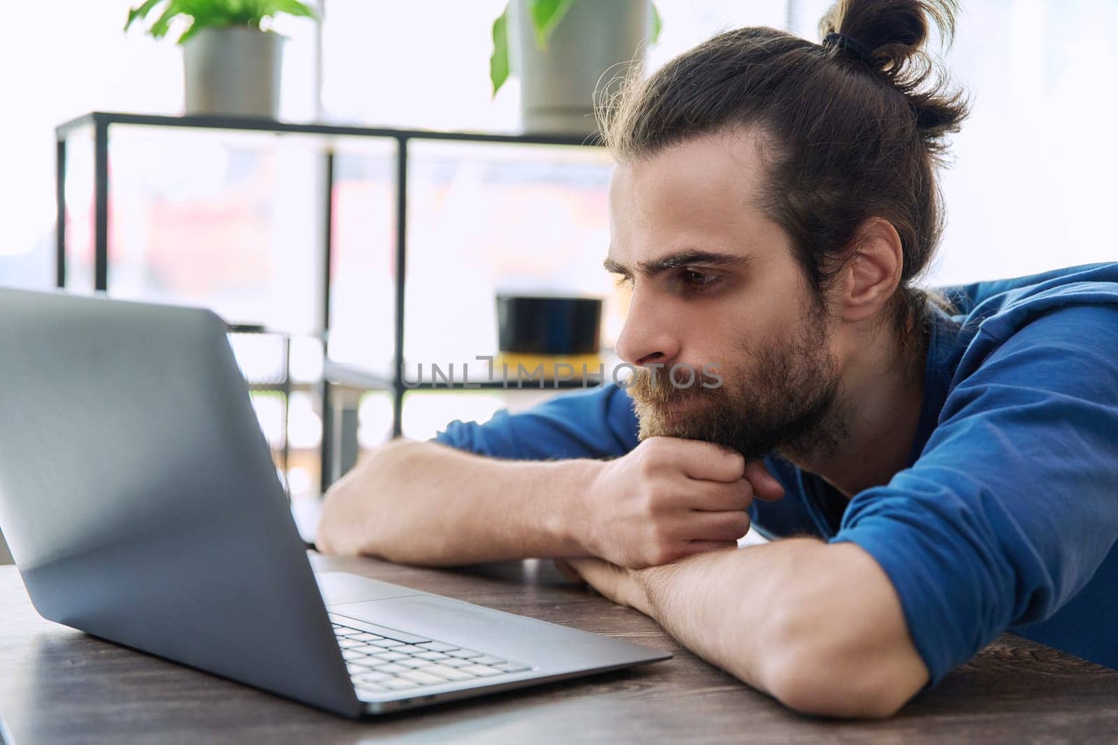 Young serious man working and studying using laptop sitting in coworking cafe. 30s handsome bearded guy looking at computer screen. Technology for leisure work business education communication people