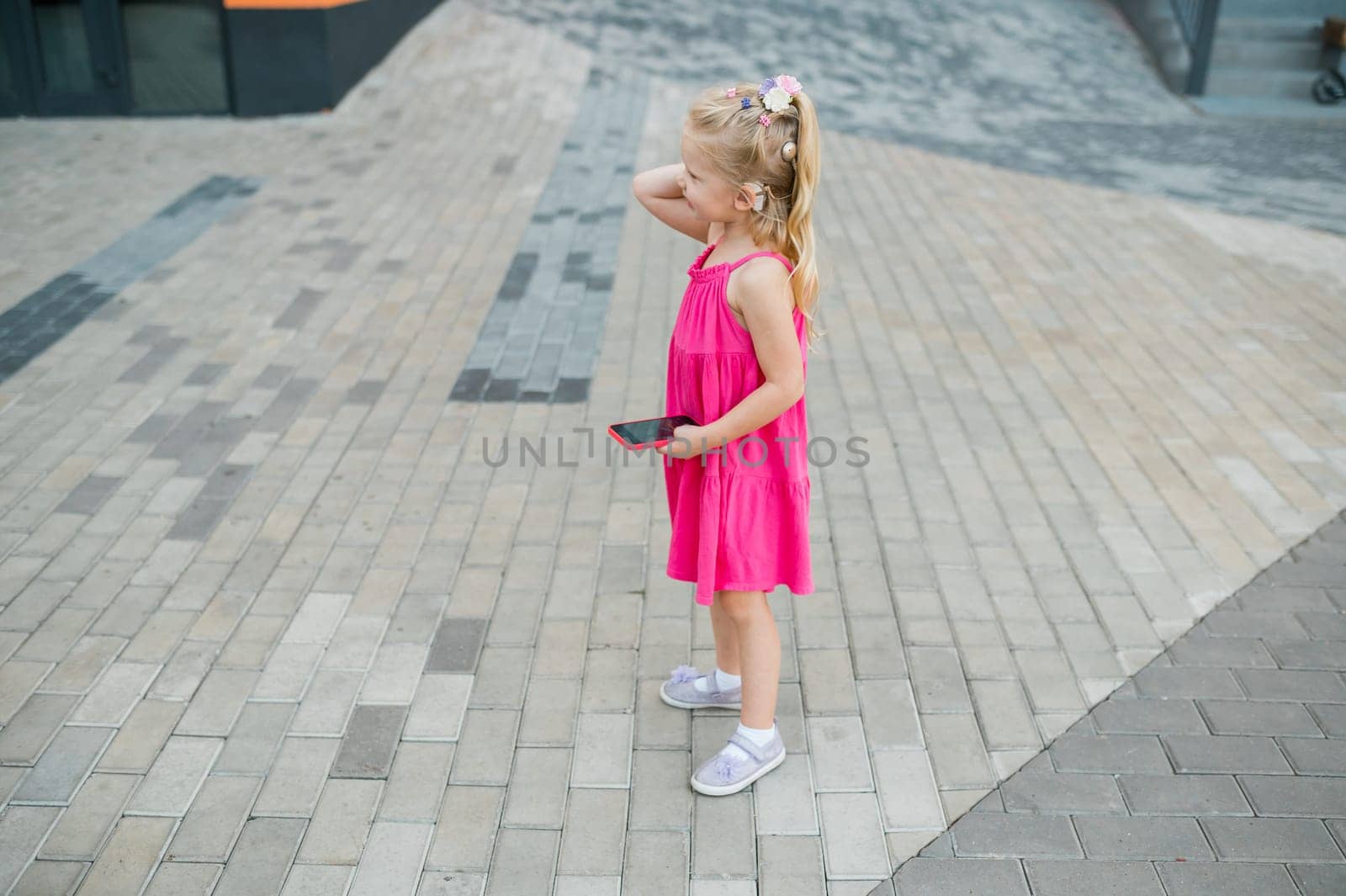 Child girl walks and have fun outdoor with cochlear implant on the head. Hearing aid and treatment concept. Copy space vertical.