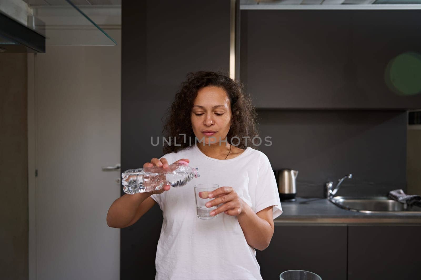 Young adult woman holding bottle of pure mineral water at home. Renewing aqua balance. Start your day with clean water for healthy diet and detox. Body care concept by artgf