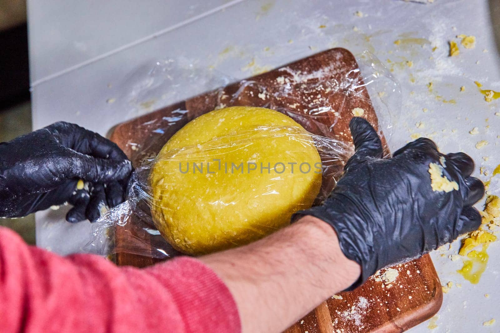 Crafting Homemade Pasta in Fort Wayne, Indiana - Close-up of gloved hands wrapping fresh, yellow dough in a bright commercial kitchen